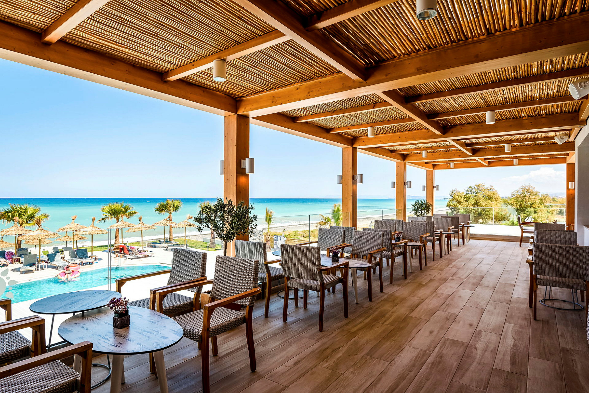 En udendørs terrasse med udsigt over en pool, parasoller og havet. (AI-genereret tekst)