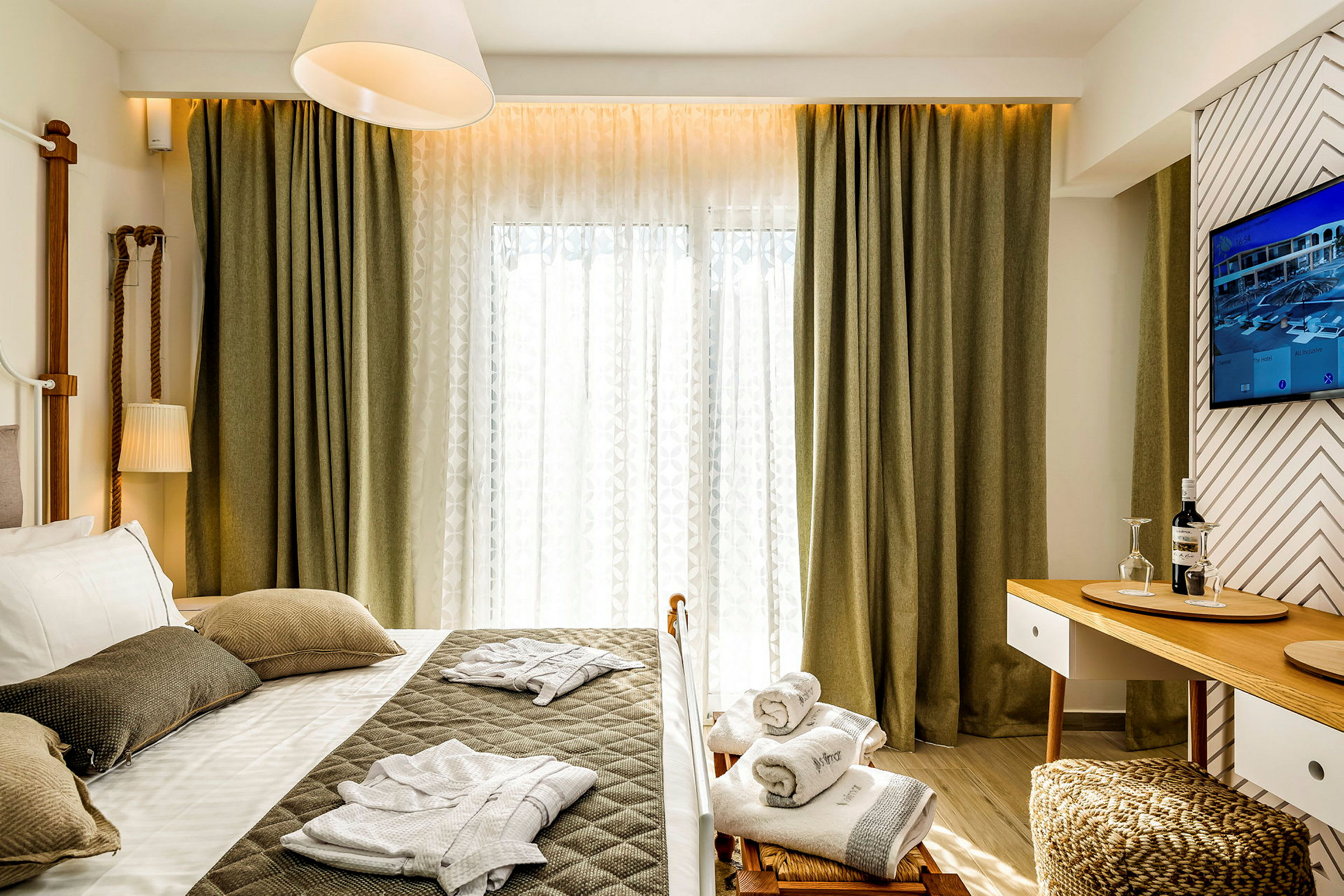 Et hotelværelse med en seng, pyntepuder og sammenlagte badekåber. Der er et bord med glas og en flaske. (AI-genereret tekst)