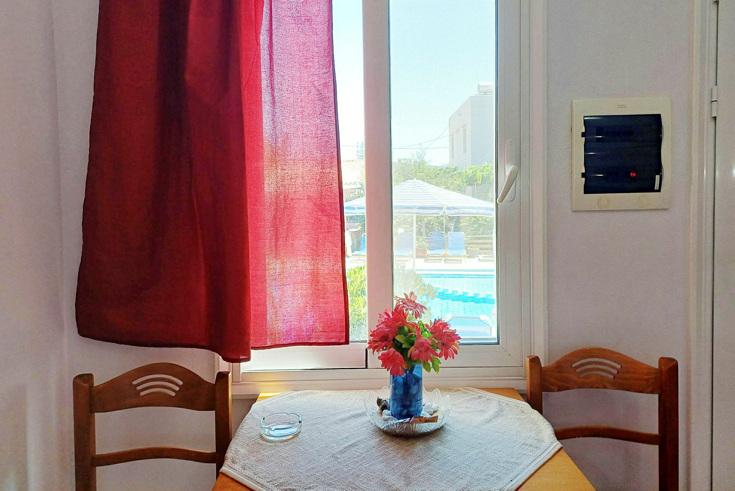 Et interiør med et bord med en vase med blomster foran et vindue med udsigt til en pool. (AI-genereret tekst)