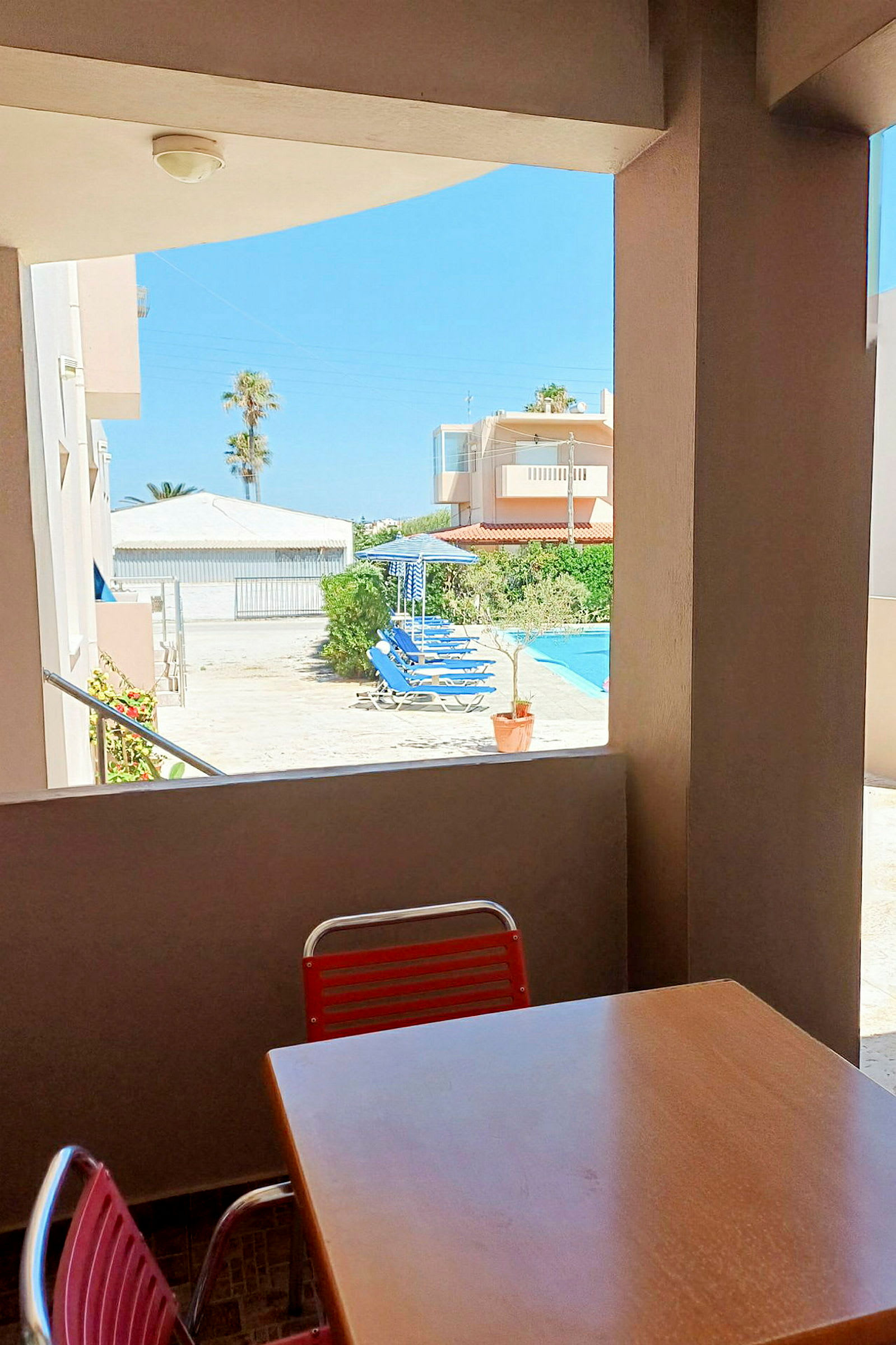 Et bord og en stol på en terrasse med udsigt til en gårdhave og en pool. (AI-genereret tekst)
