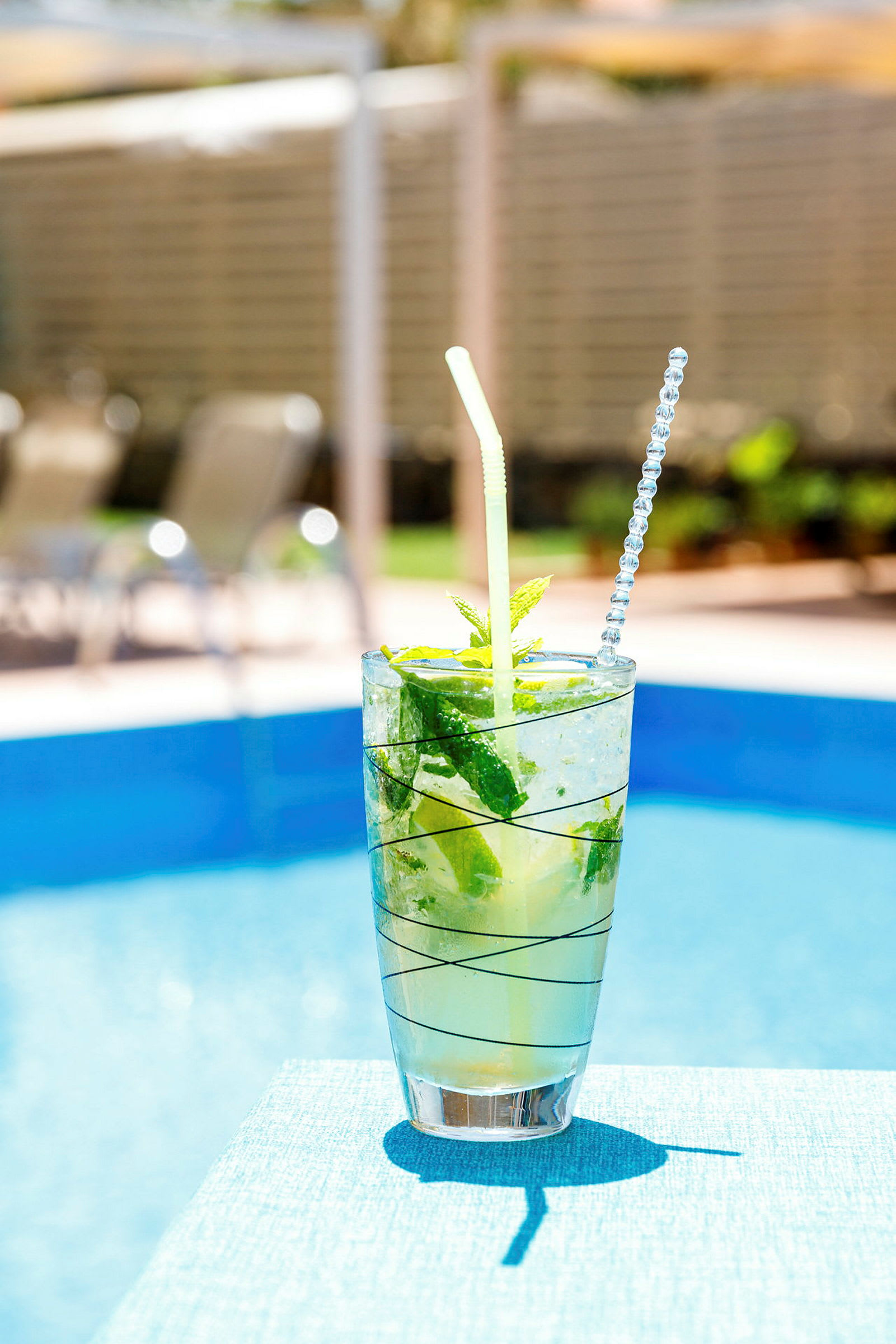En glasdrink med is, mynte og lime ved en pool. (AI-genereret tekst)