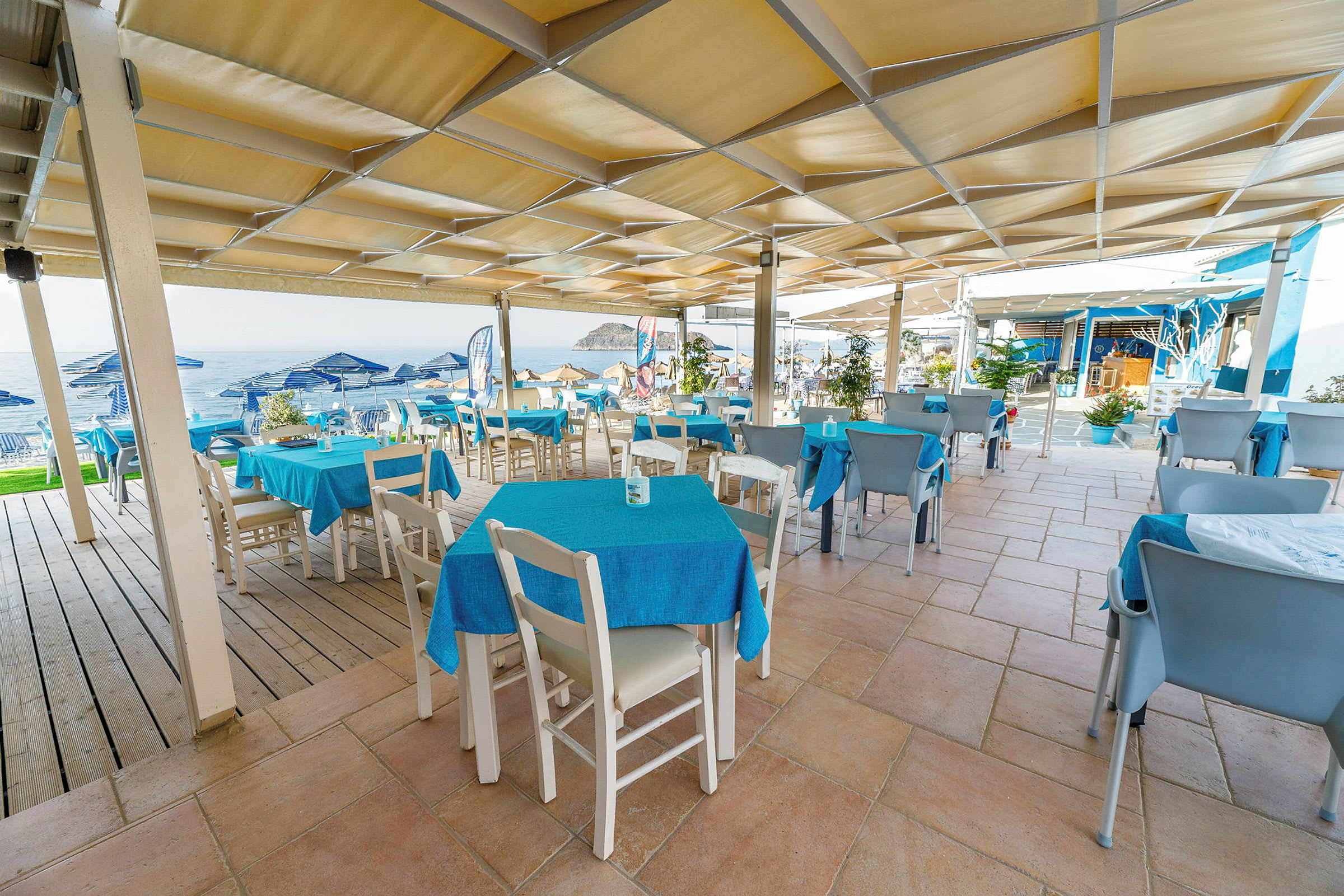 Udendørsrestaurant med blå duge og udsigt til havet. (AI-genereret tekst)