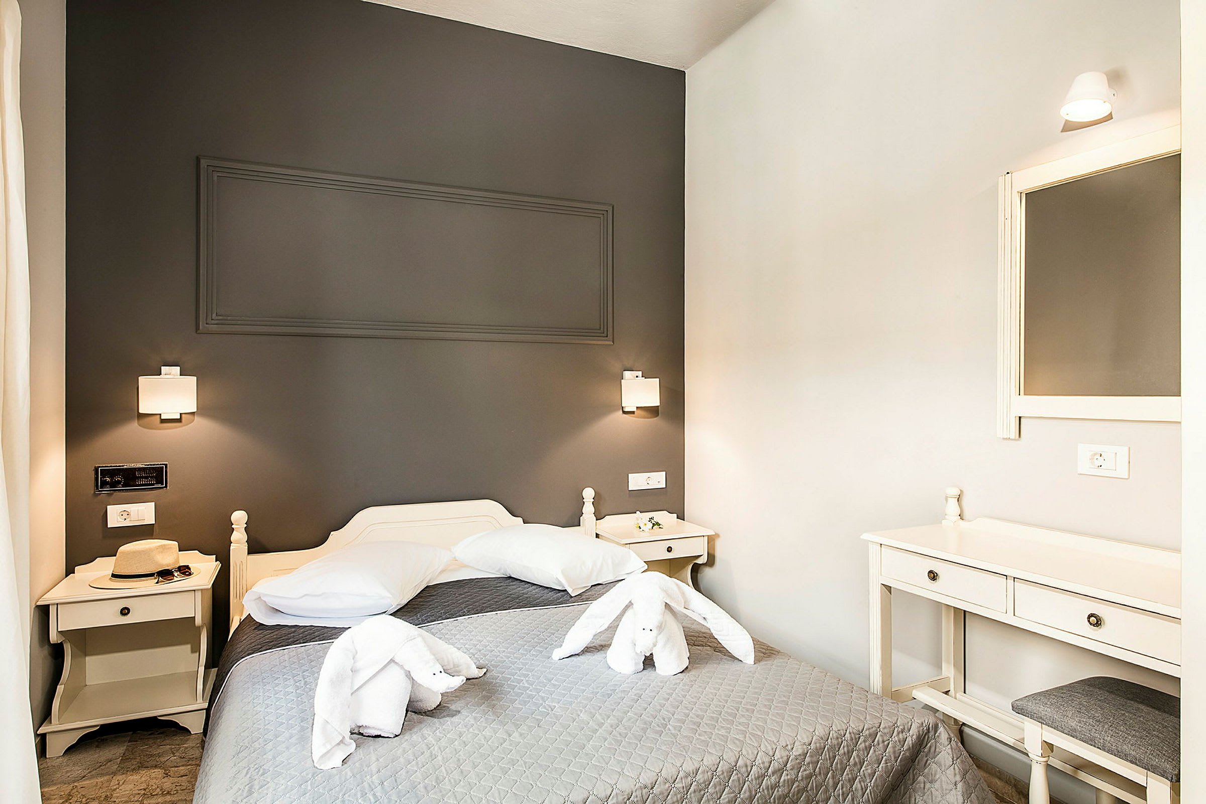 Et hotelværelse med en seng, natbord og spejl. Håndklæder er foldet som en dekorativ kanin på sengen. (AI-genereret tekst)