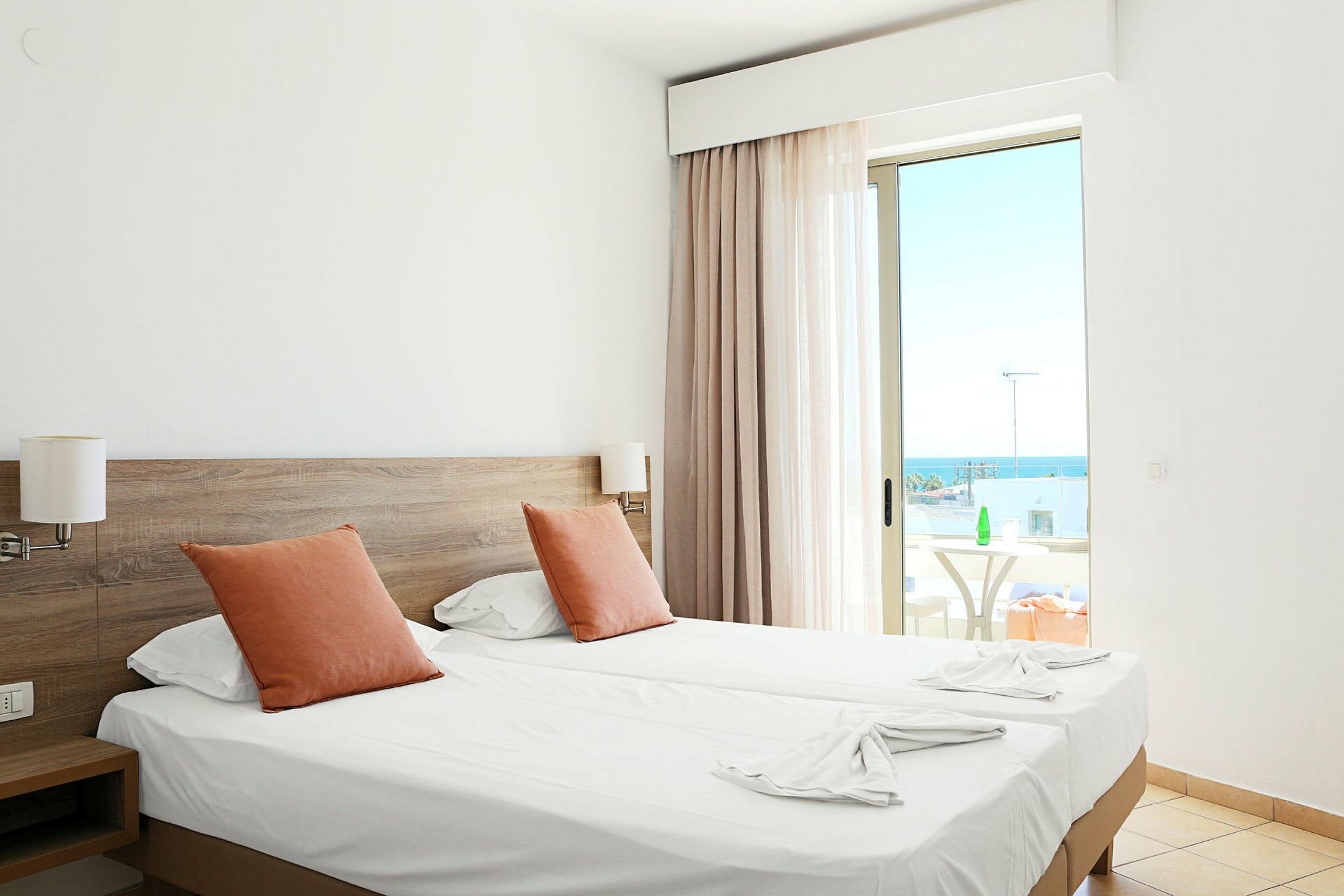 Hotelværelse med to enkeltsenge, orange puder og en altan med havudsigt. (AI-genereret tekst)
