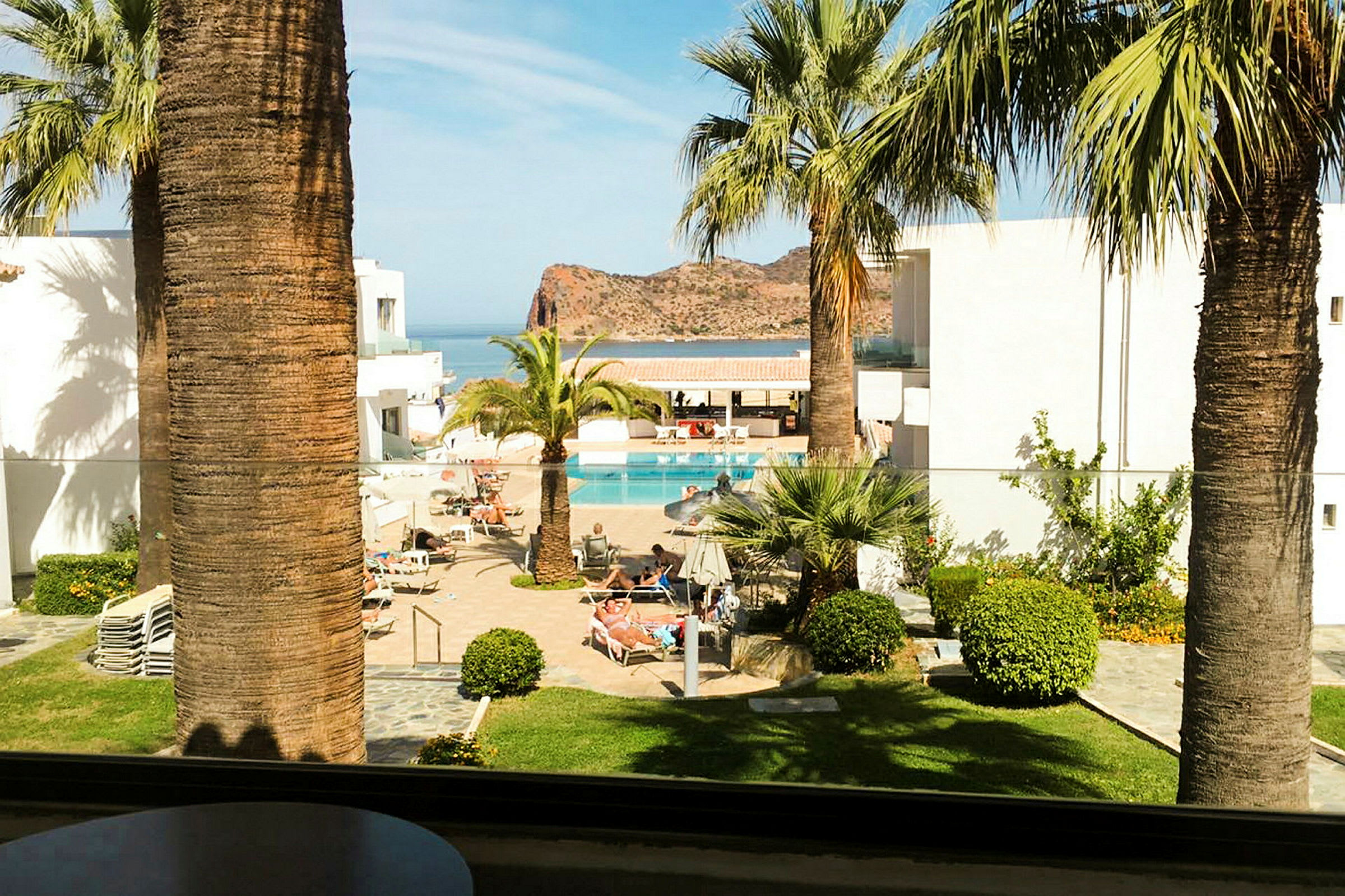 Hotelområde med pool og palmer, udsigt over havet og klipper i baggrunden. (AI-genereret tekst)