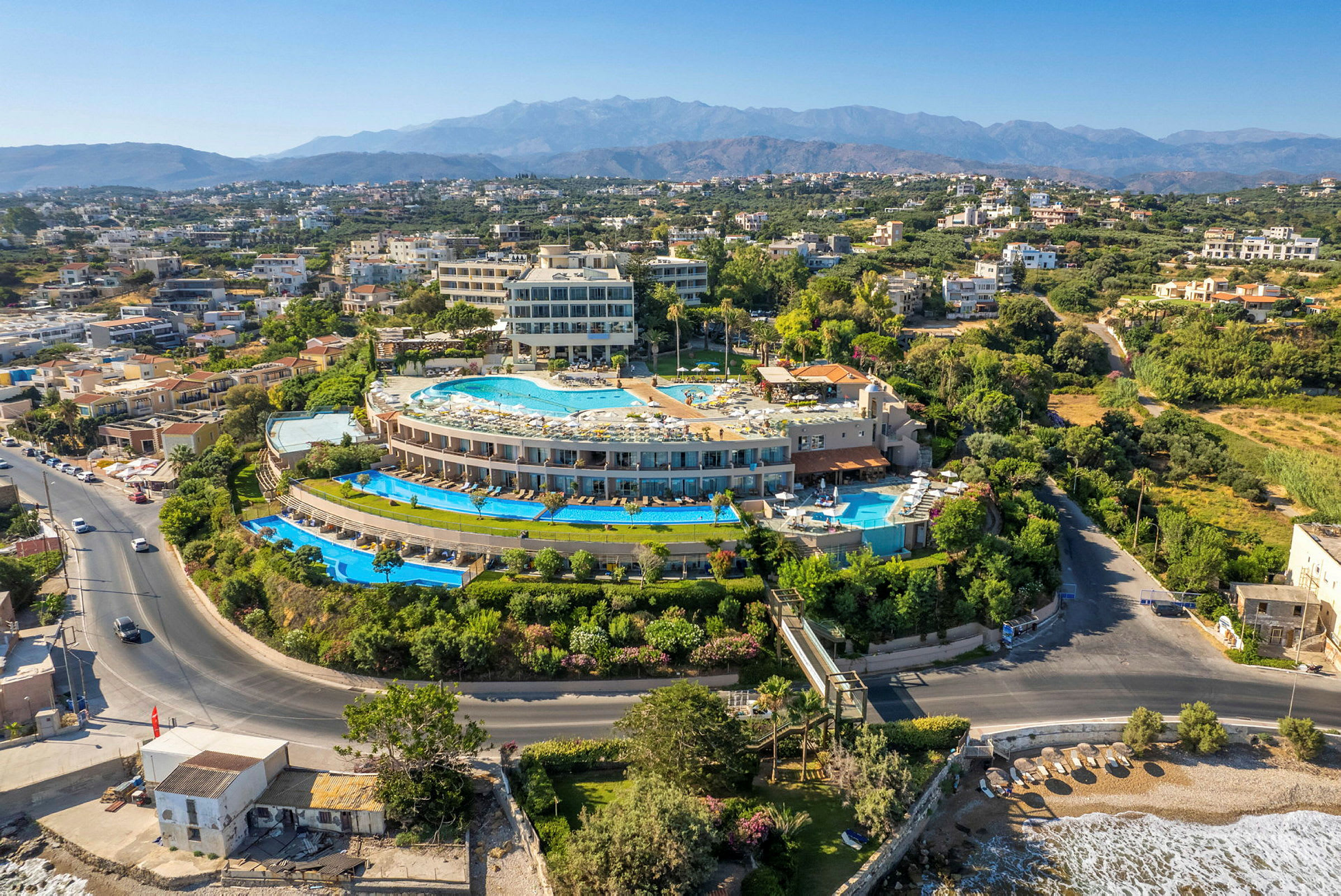 Luftfoto af et hotelområde med pools, omgivet af andre bygninger og grønne områder. (AI-genereret tekst)