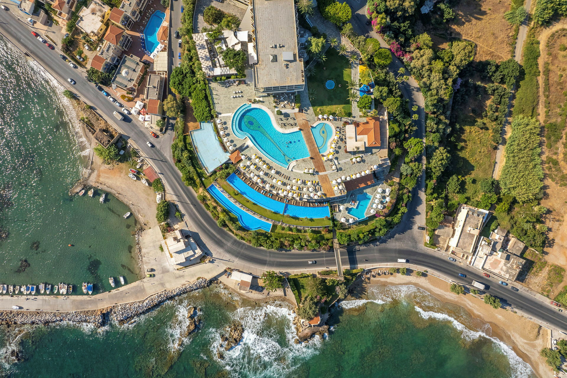 Luftfoto af hotelområde med swimmingpools ved siden af havet. (AI-genereret tekst)