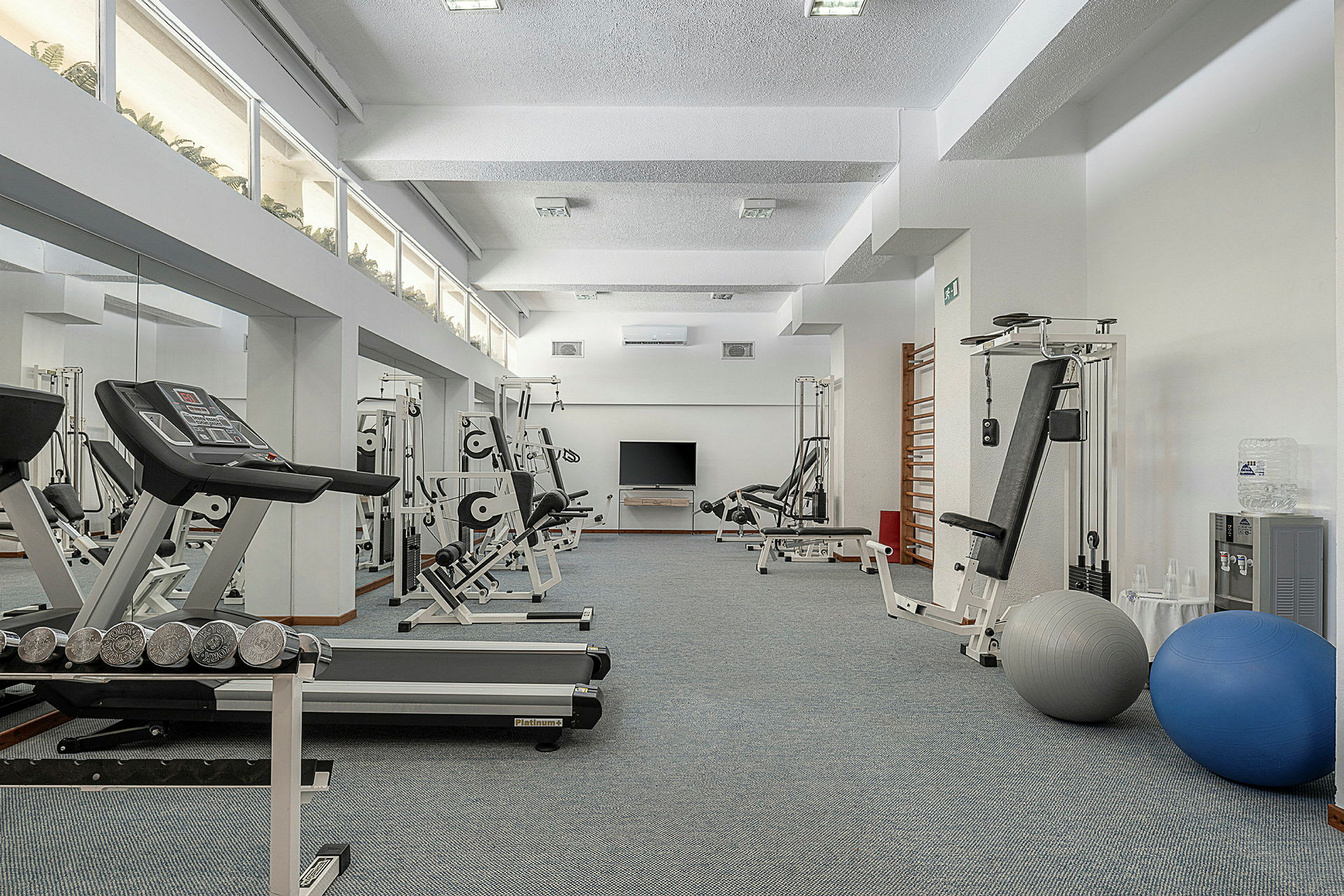 Billedet viser et fitnesscenter med forskellige træningsredskaber såsom løbebånd og styrketræningsmaskiner. (AI-genereret tekst)