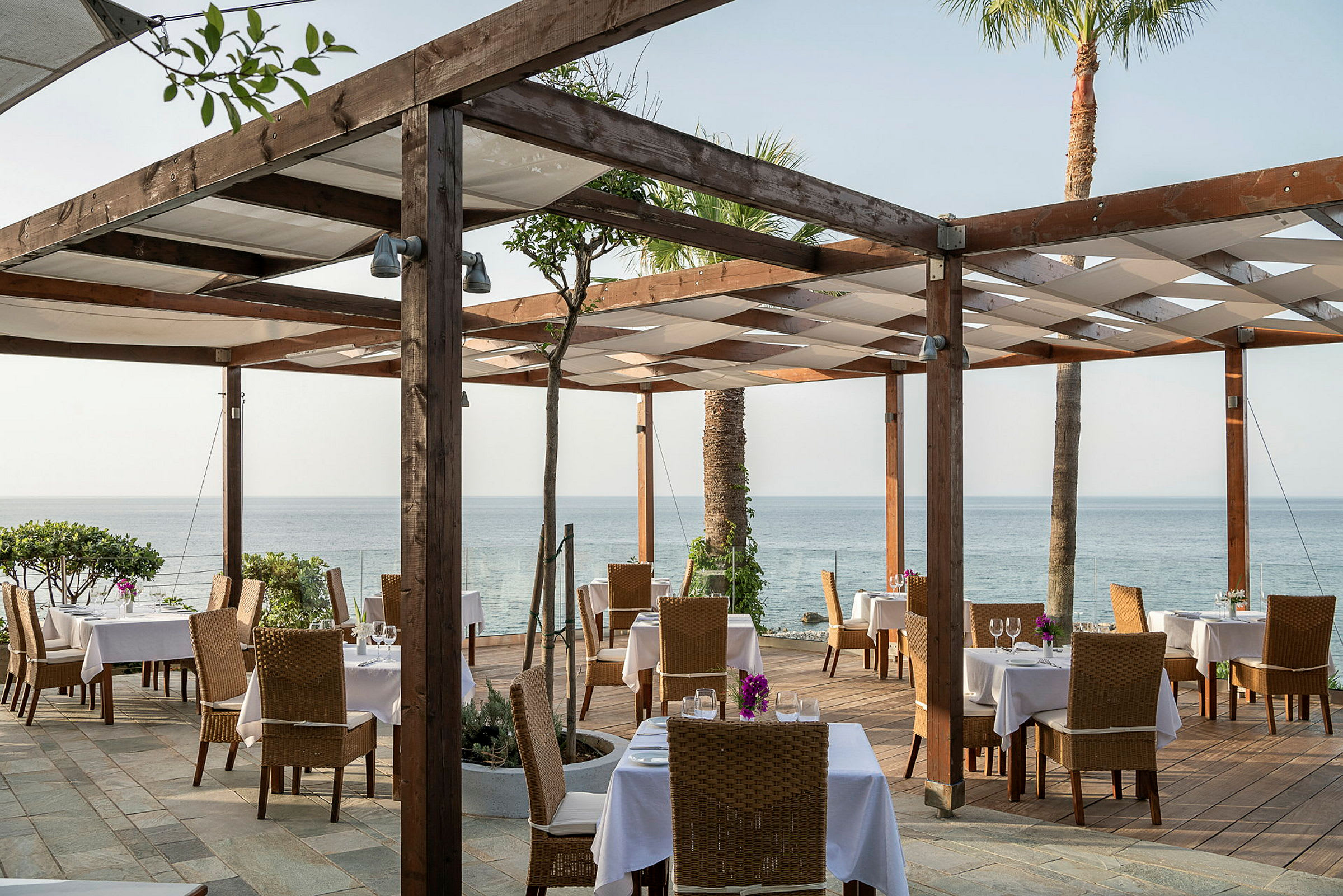 Restaurant med udendørs servering, borde og stole, og udsigt over havet. (AI-genereret tekst)