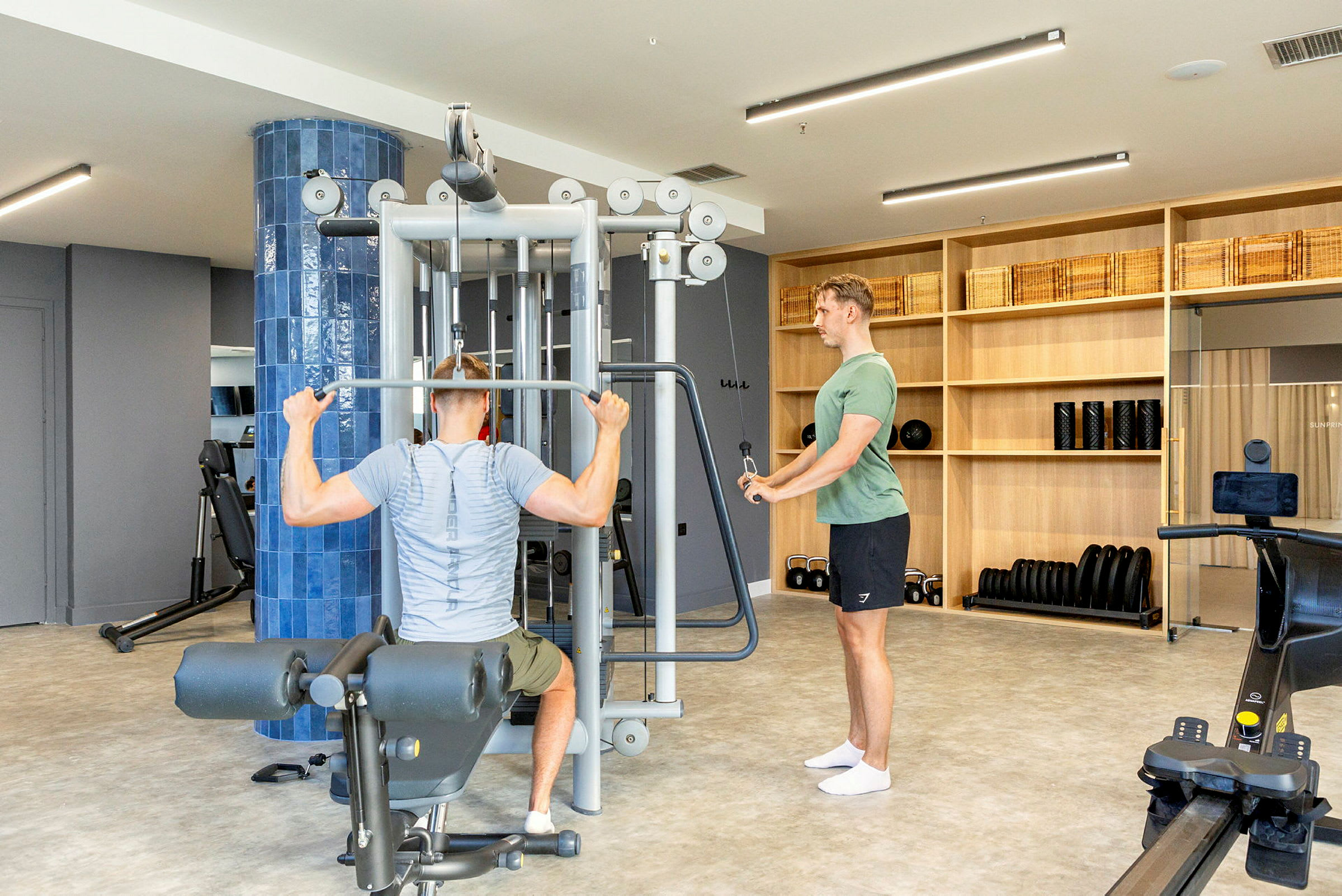Træningsudstyr i et fitnesscenter med personer, der anvender en træningsmaskine. (AI-genereret tekst)