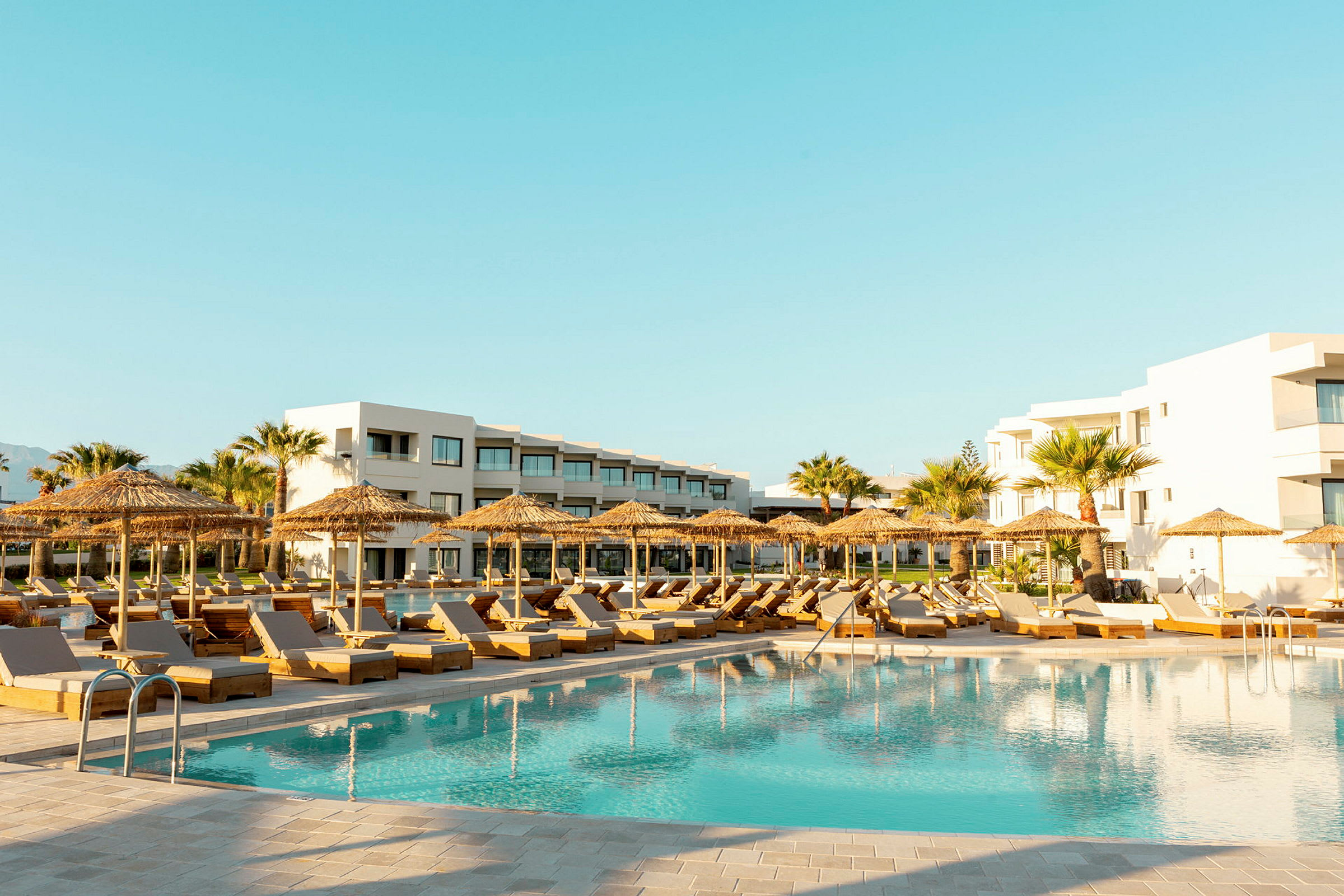 Poolområde med liggestole, parasoller og moderne hotelbygninger i baggrunden. (AI-genereret tekst)