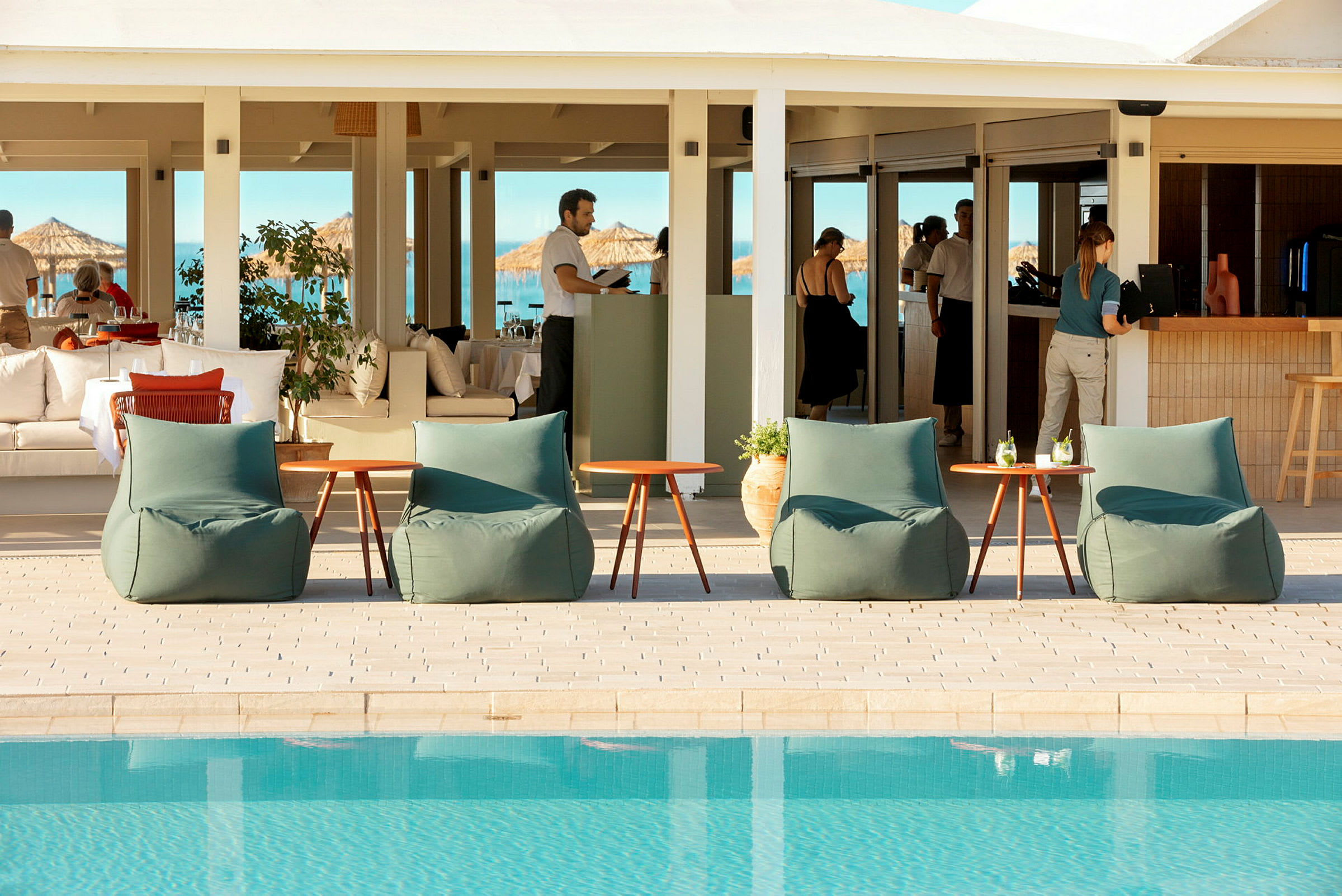 Udendørsmøbler ved en pool med en restaurant i baggrunden. (AI-genereret tekst)