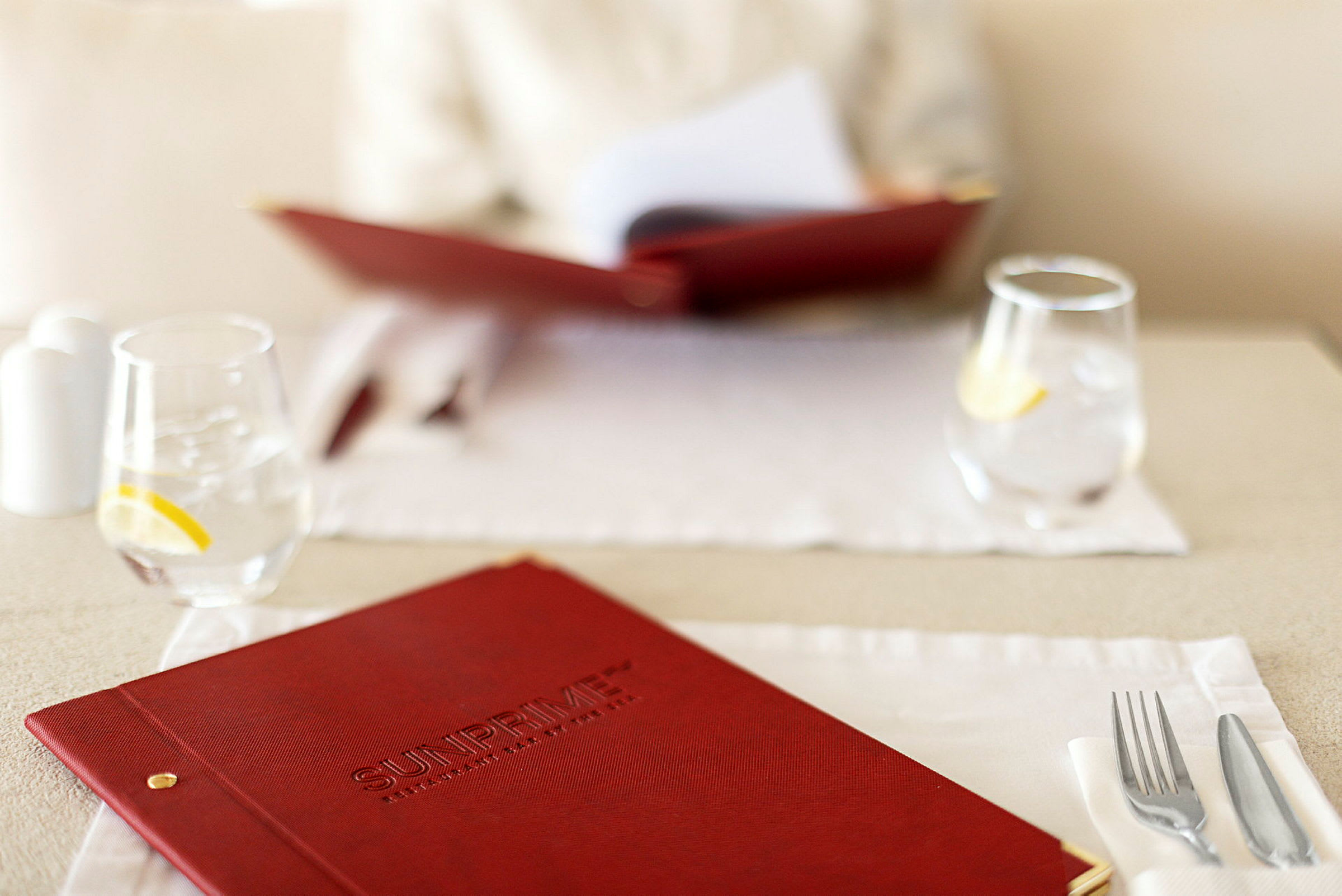 Nærbillede af en rød menubog på et dækket restaurantbord med glas og bestik. (AI-genereret tekst)