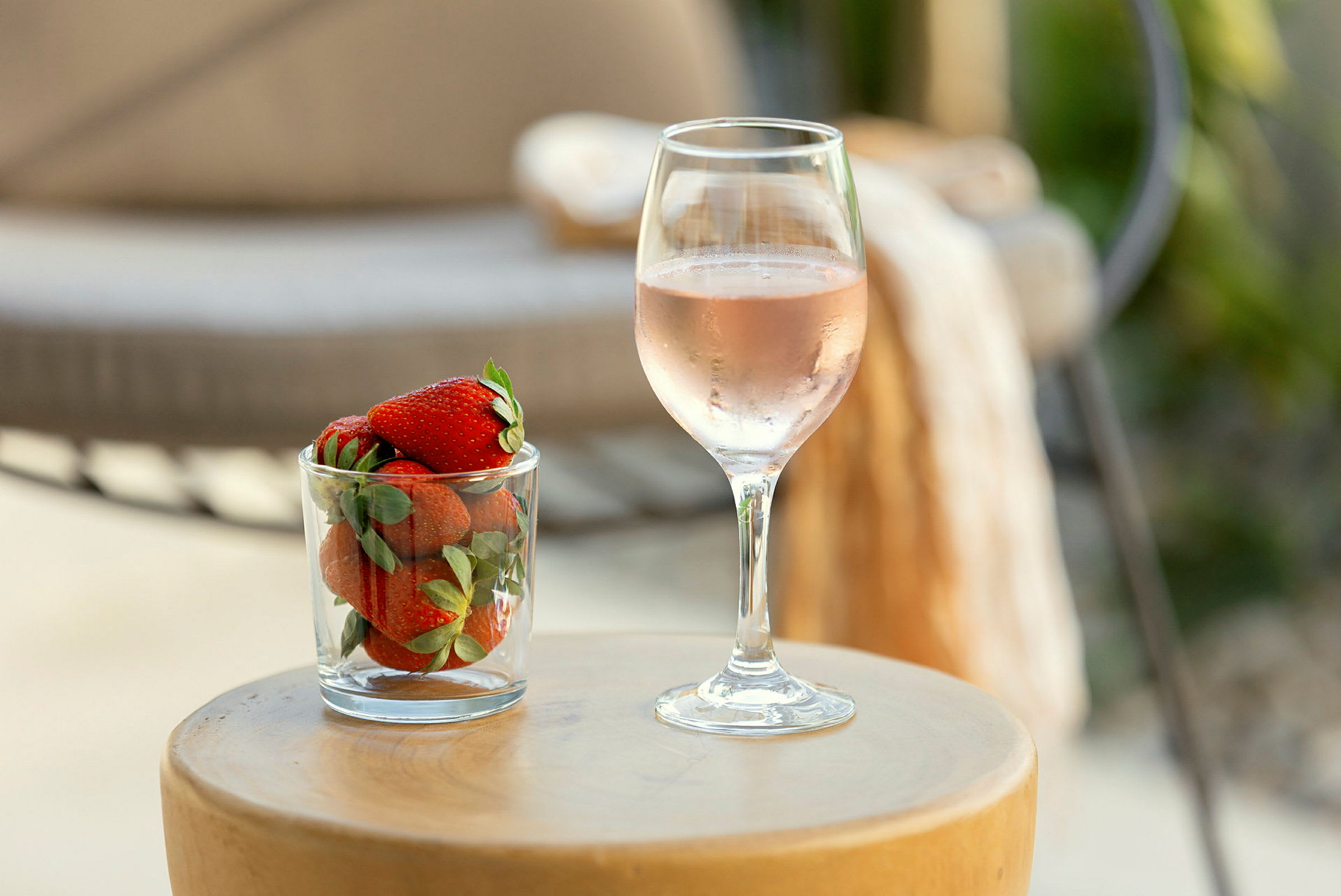 Et glas med jordbær ved siden af et glas rosévin står på et rundt bord. (AI-genereret tekst)