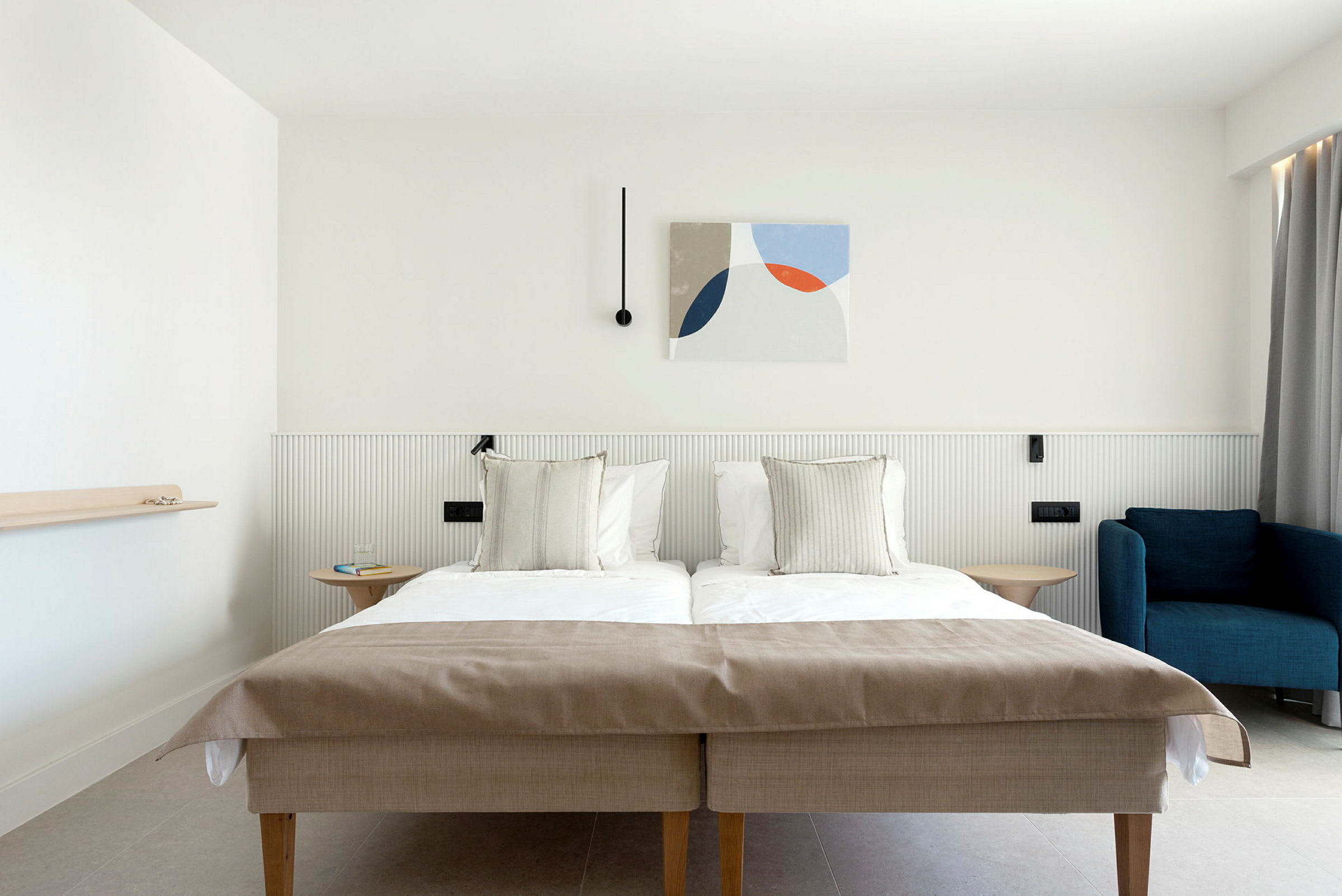 Et hotelværelse med en dobbeltseng, en blå lænestol og moderne vægdekoration. (AI-genereret tekst)