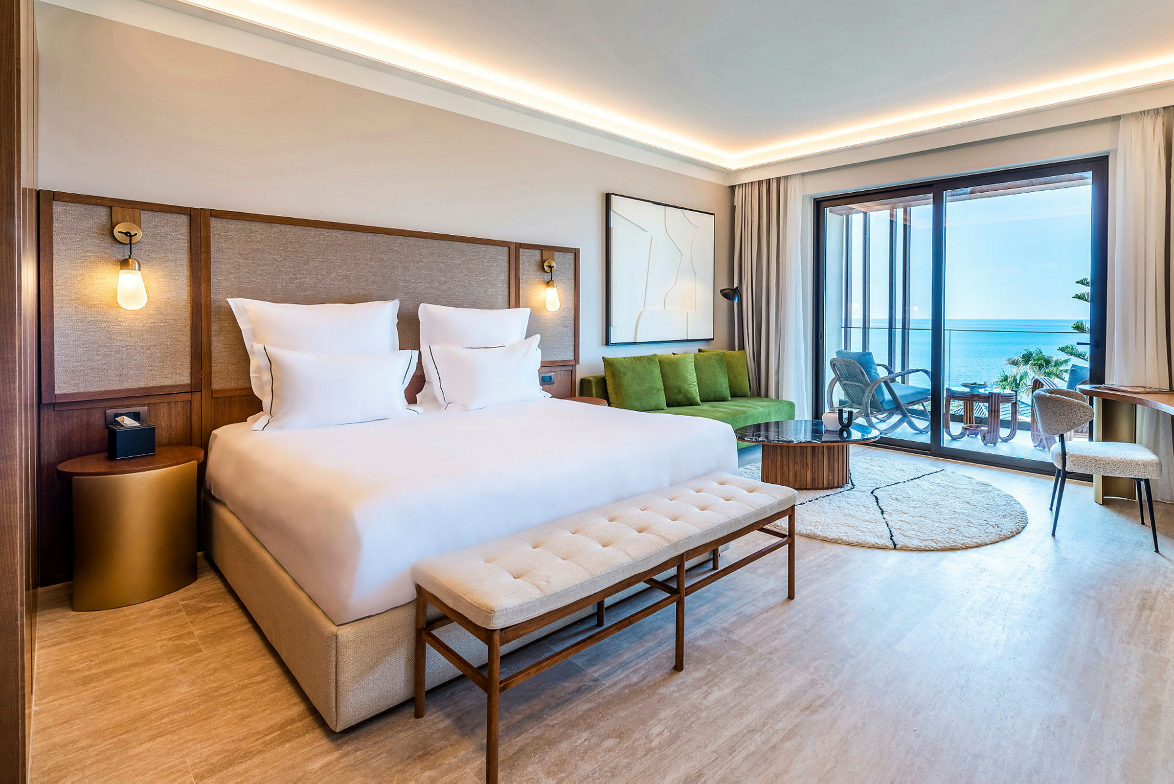 Et moderne hotelværelse med en dobbeltseng og udsigt over havet fra en møbleret balkon. (AI-genereret tekst)