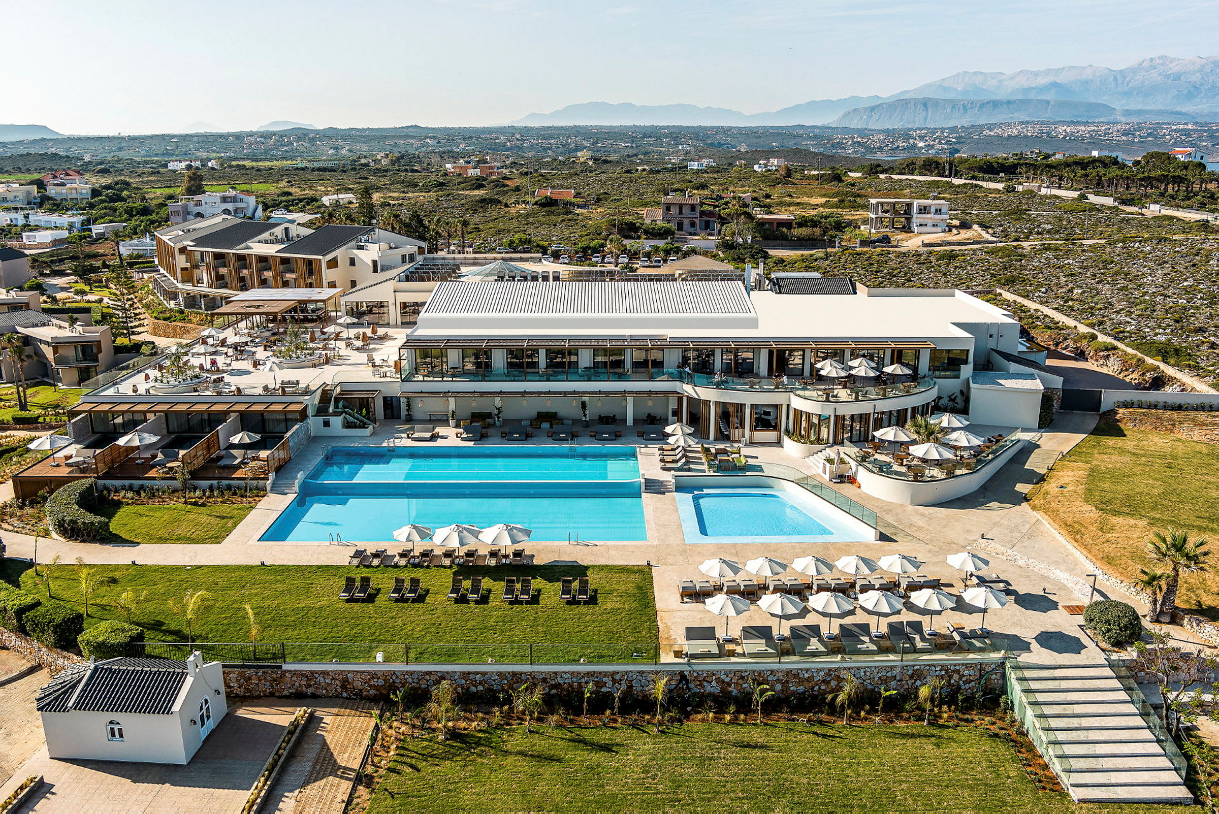 Luftfoto af et luksuriøst resort med poolområde, grønne områder og omgivende landskab. (AI-genereret tekst)