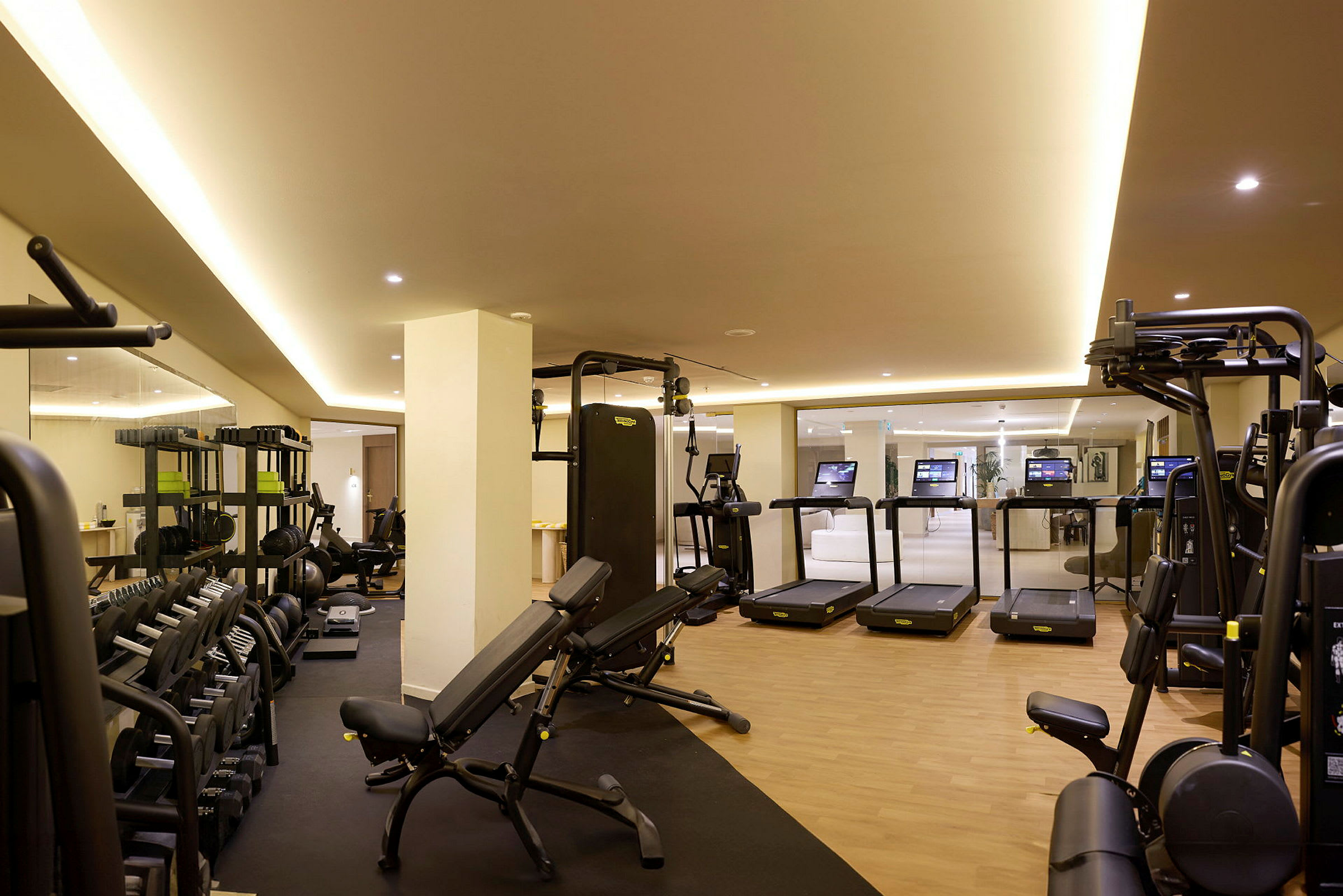 Et fitnesscenter med træningsmaskiner, løbebånd og vægte i et lyst interiør. (AI-genereret tekst)