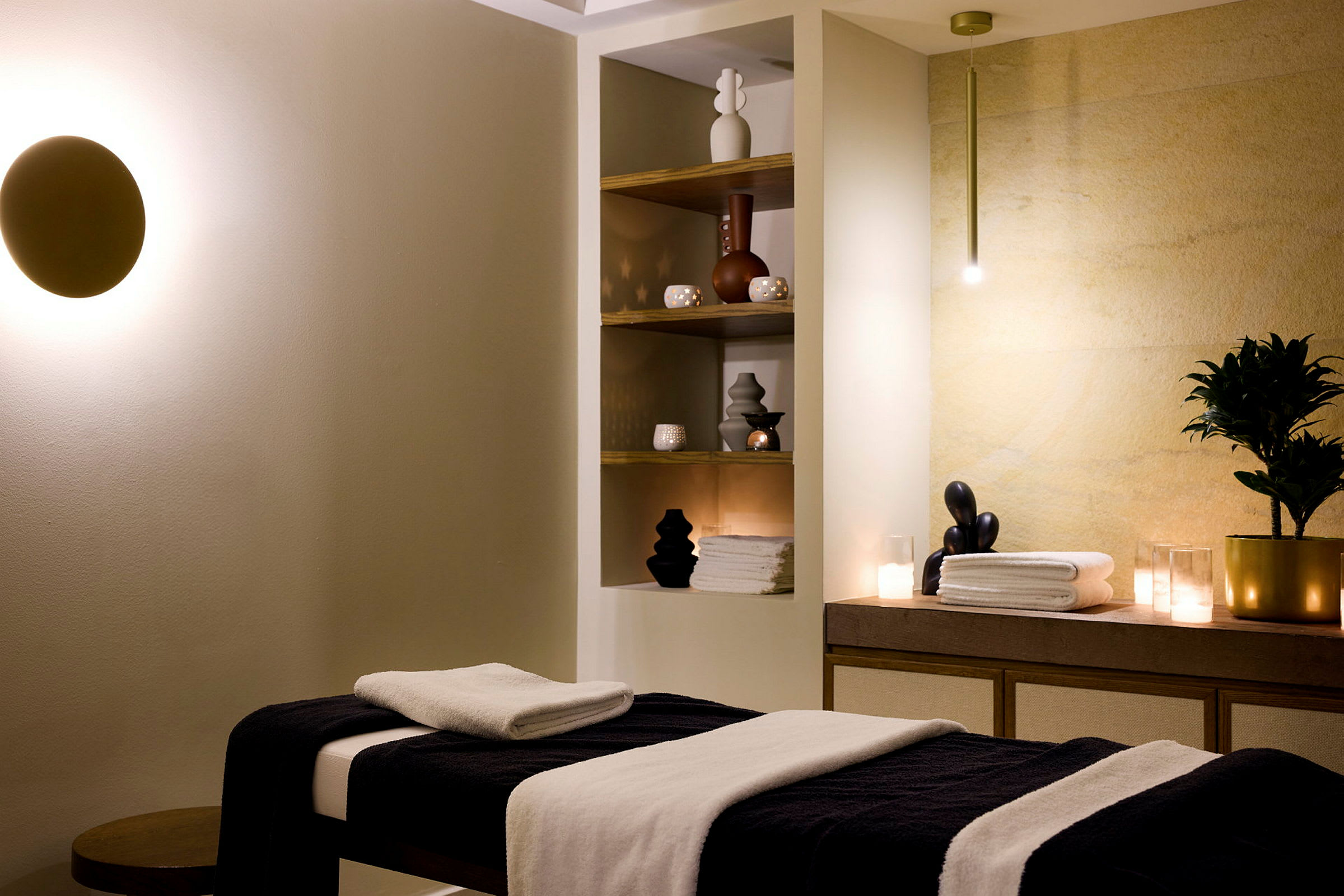 Et spa-rum med massagebord, hylder med dekorationer og håndklæder samt blød belysning. (AI-genereret tekst)