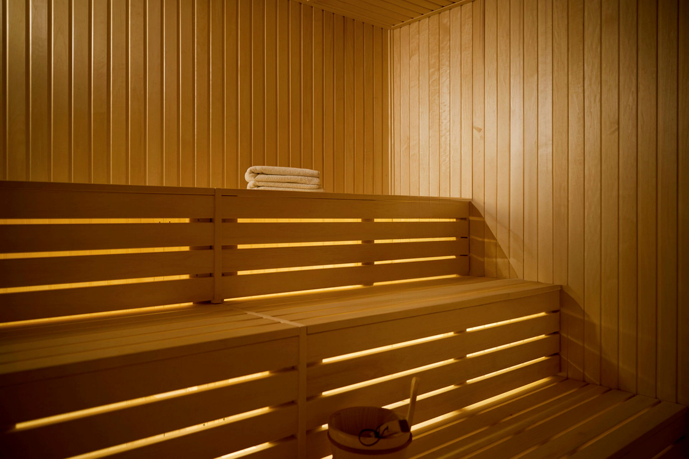 Et interiør af en traditionel sauna med træpaneler og træsædebænke, hvor et hvidt sammenfoldet håndklæde ligger på den øverste bænk. (AI-genereret tekst)