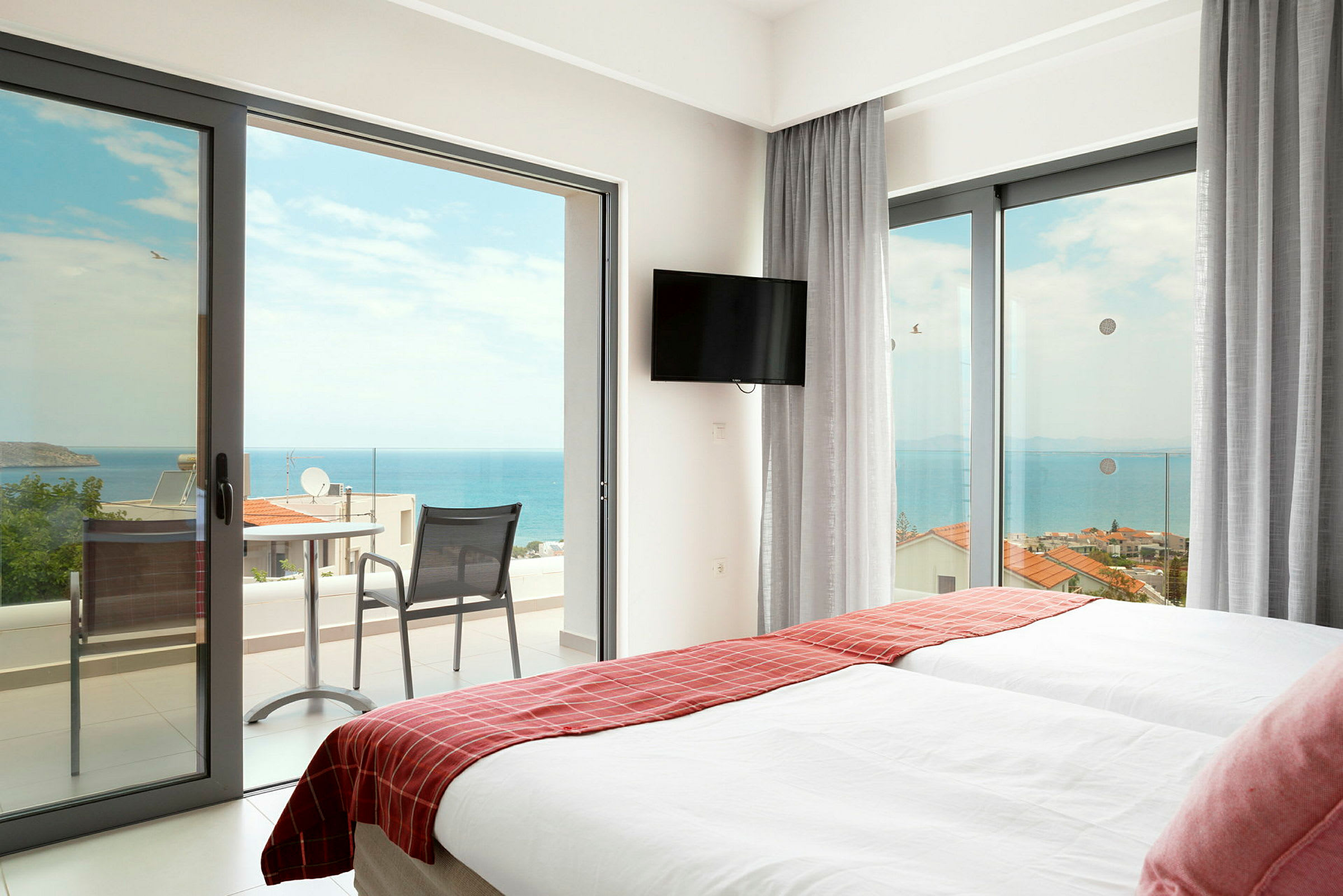 Hotelværelse med to senge og døre til balkon mod havet. (AI-genereret tekst)