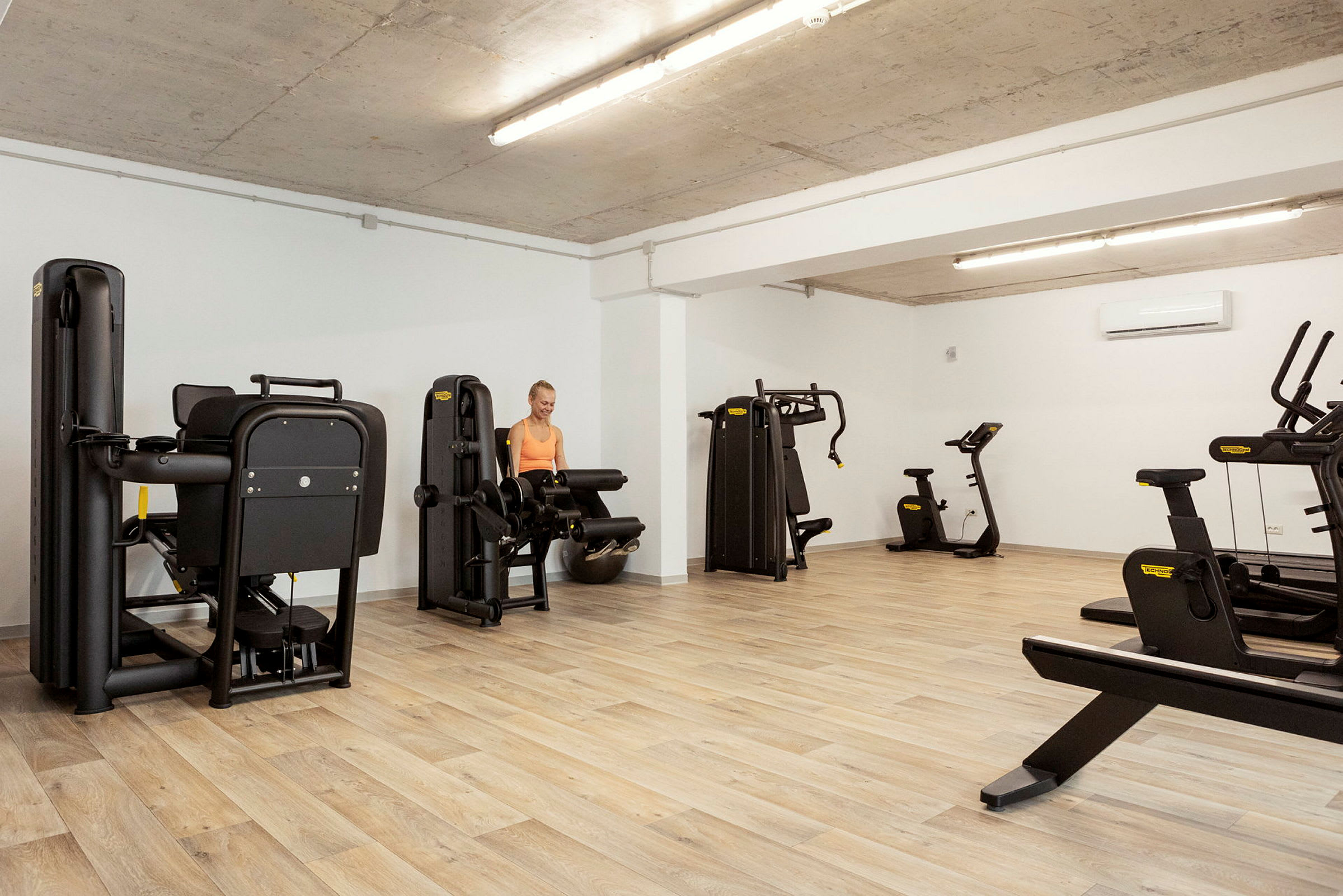 Et fitnesscenter med trægulv og forskellige træningsmaskiner. (AI-genereret tekst)