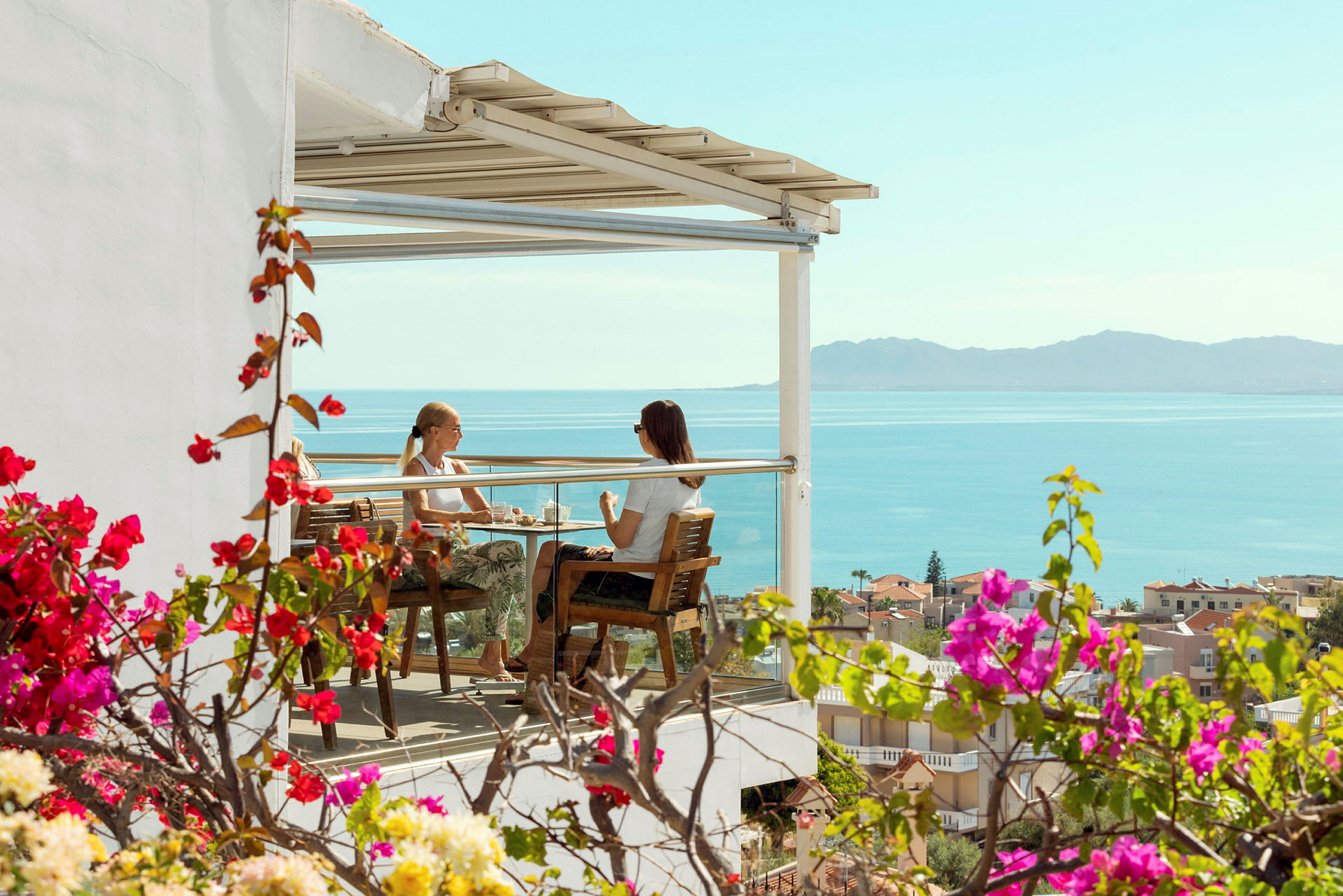 To personer sidder på en terrasse med udsigt over havet. (AI-genereret tekst)