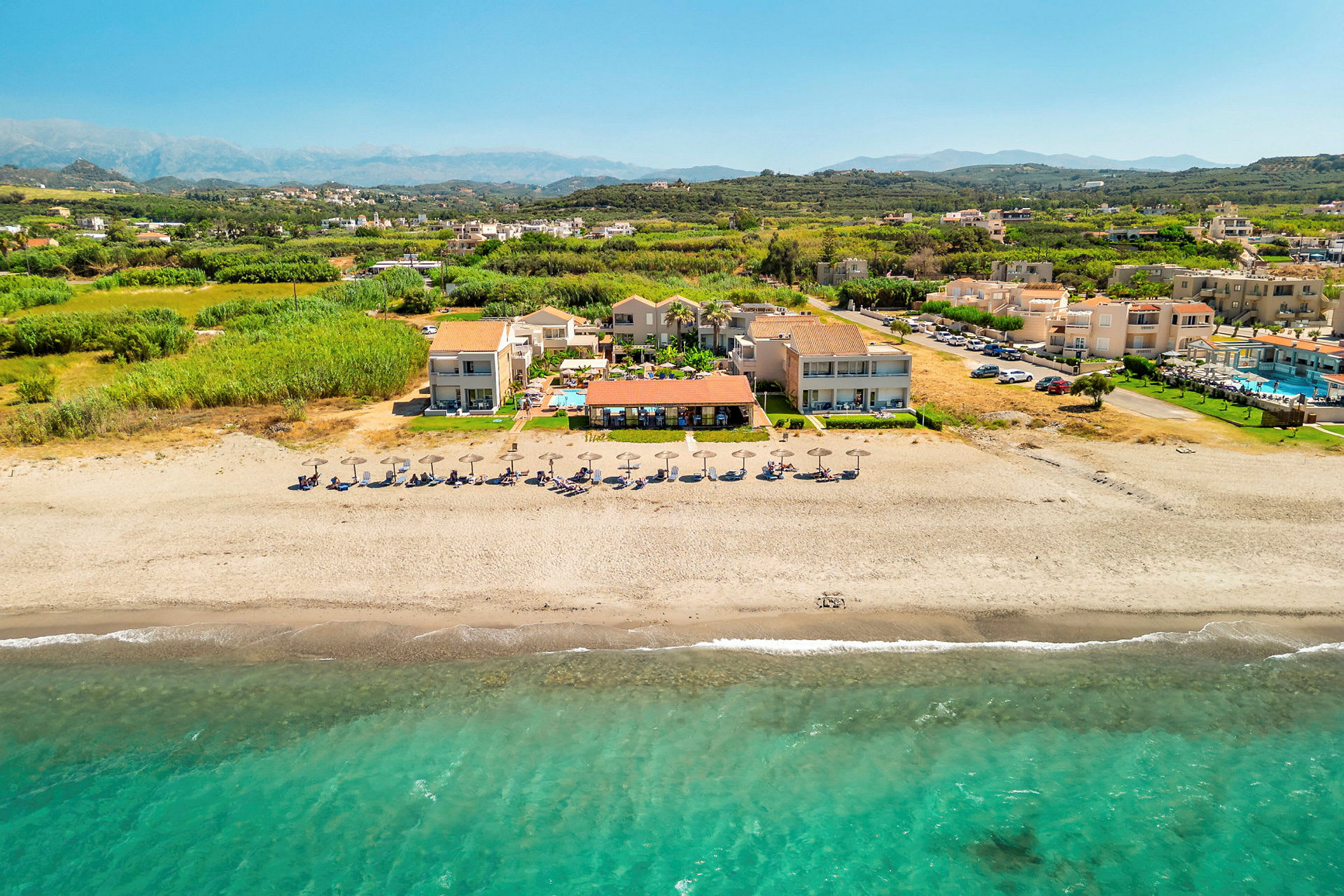 Luftfoto af strand med parasoller og ferieanlæg. (AI-genereret tekst)