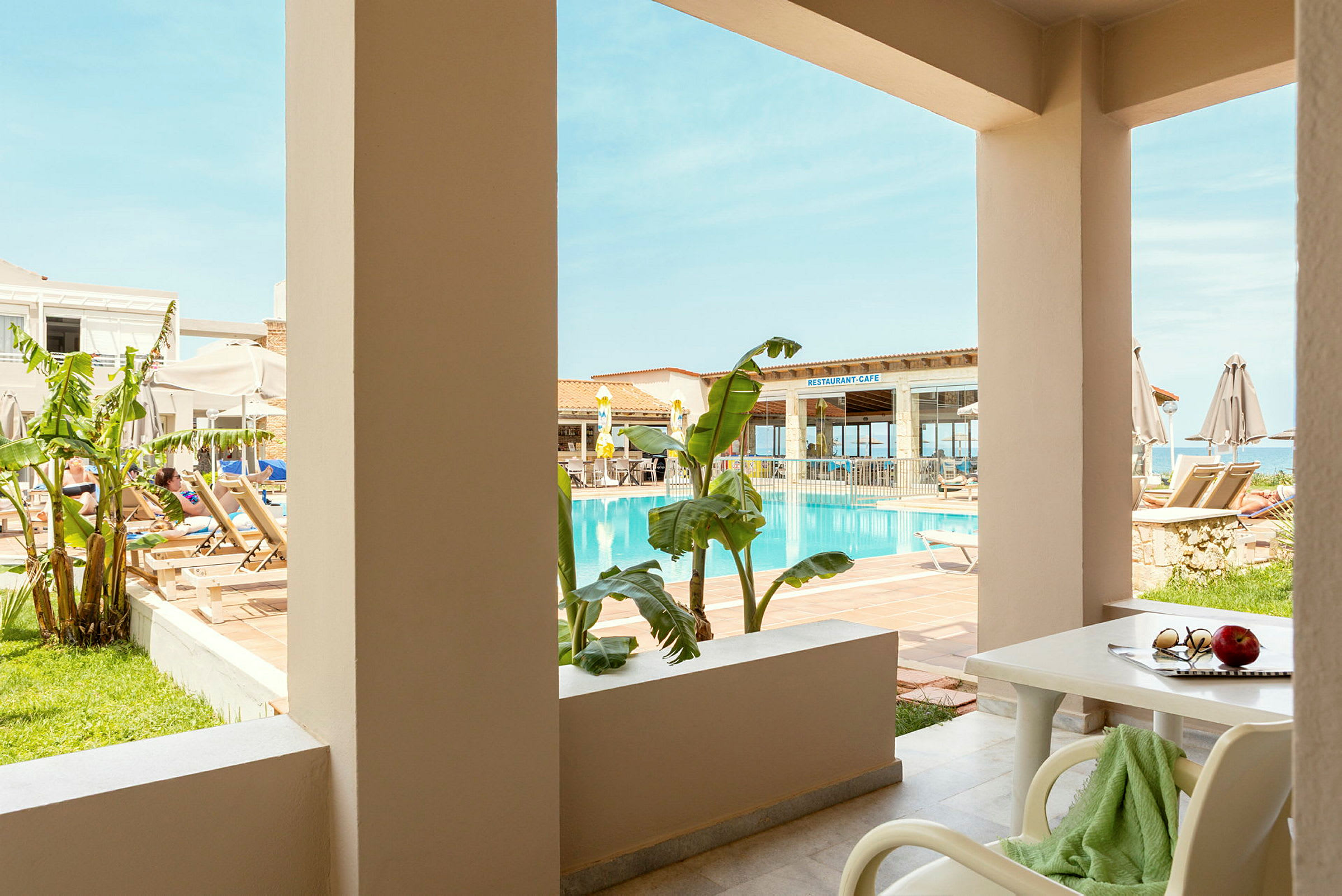 Billedet viser en terrasse med udsigt til en swimmingpool og en restaurant i baggrunden. (AI-genereret tekst)