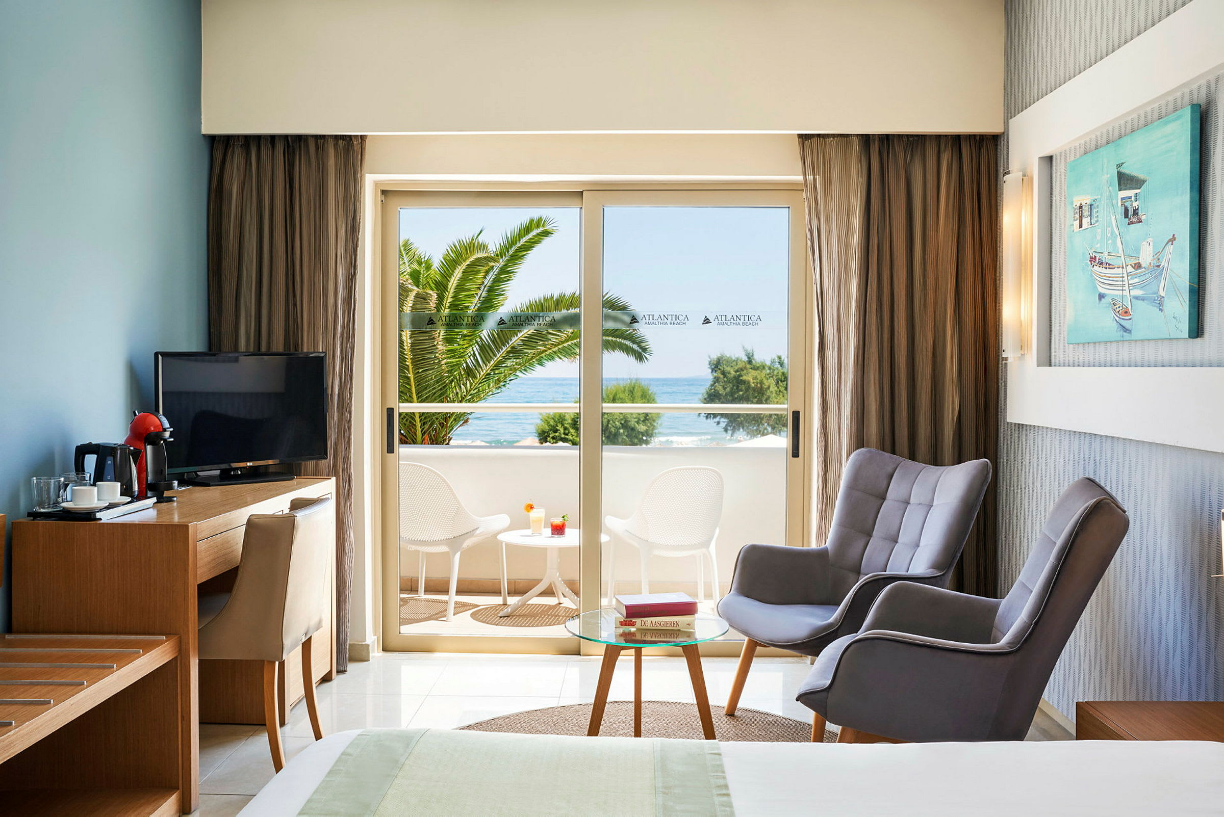 Hotelværelse med siddeområde og udsigt til altan med bord og stole samt havudsigt. (AI-genereret tekst)