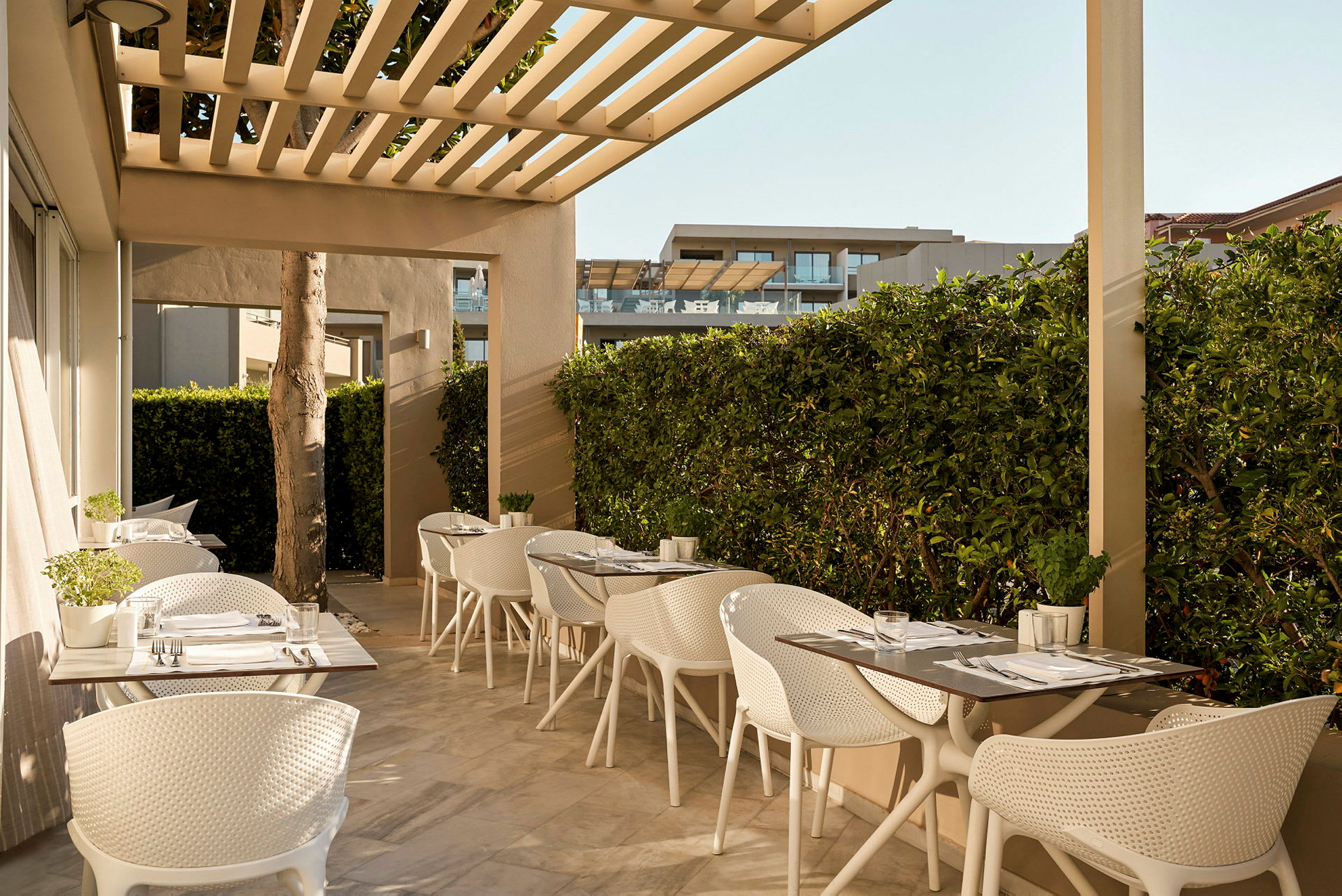 En udendørs siddegruppe med hvide stole ved borde på en terrasse. (AI-genereret tekst)