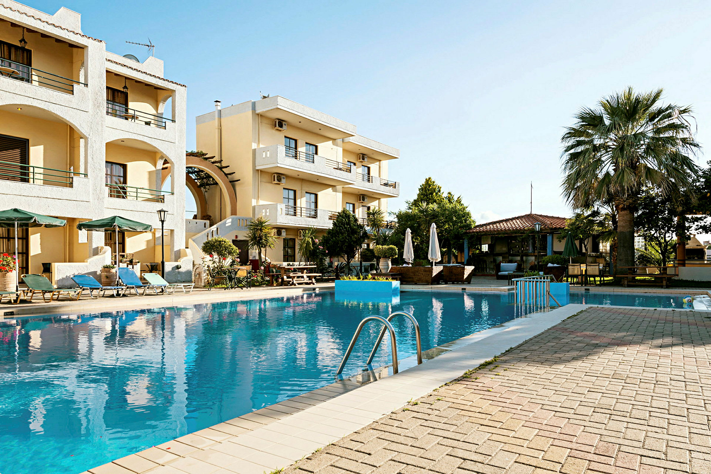 Udsigt over en pool omgivet af solsenge og et hotel i baggrunden. (AI-genereret tekst)