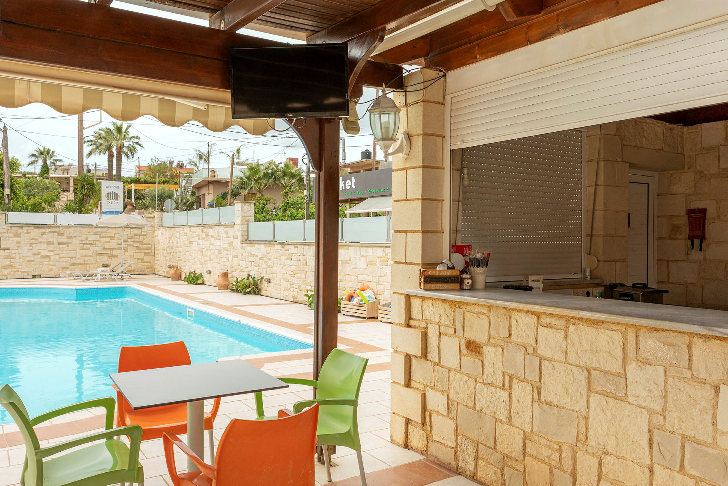 Udendørsområde med swimmingpool, borde og stole samt en bar med stenfacade. (AI-genereret tekst)
