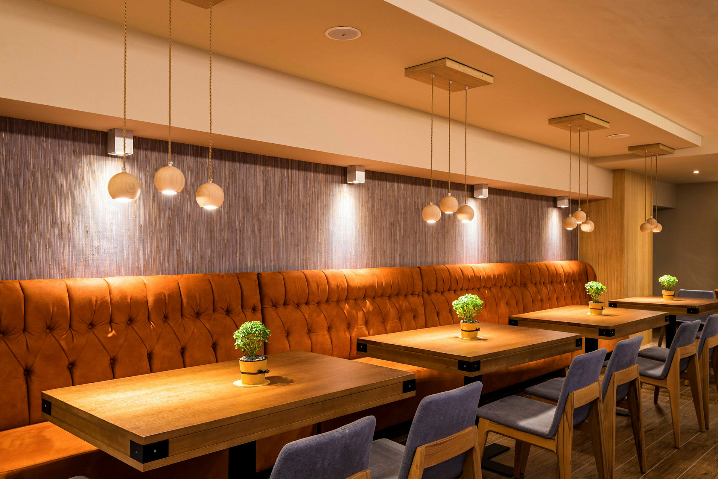 Interiør af en restaurant med orange polstrede bænke og borde dekoreret med små grønne planter. (AI-genereret tekst)