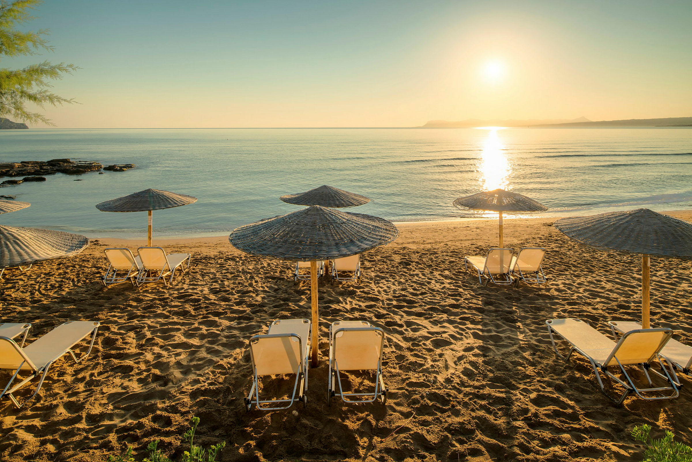 Strand med parasoller og solsenge ved solnedgang. (AI-genereret tekst)