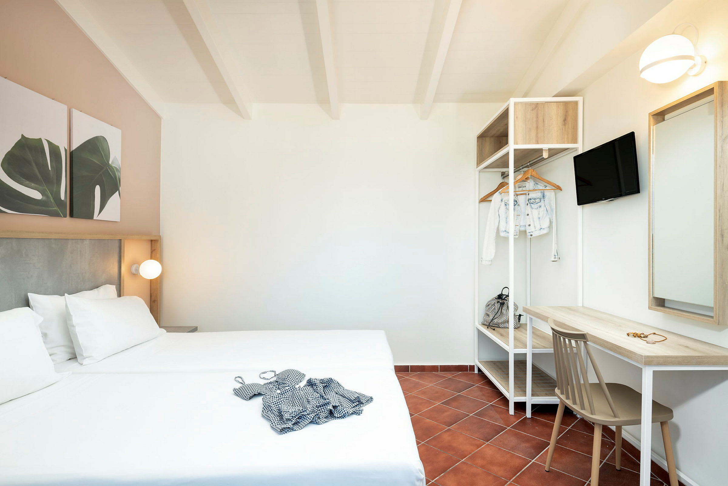 Et hotelværelse med dobbeltseng, skrivebord, stol og åben garderobe. (AI-genereret tekst)