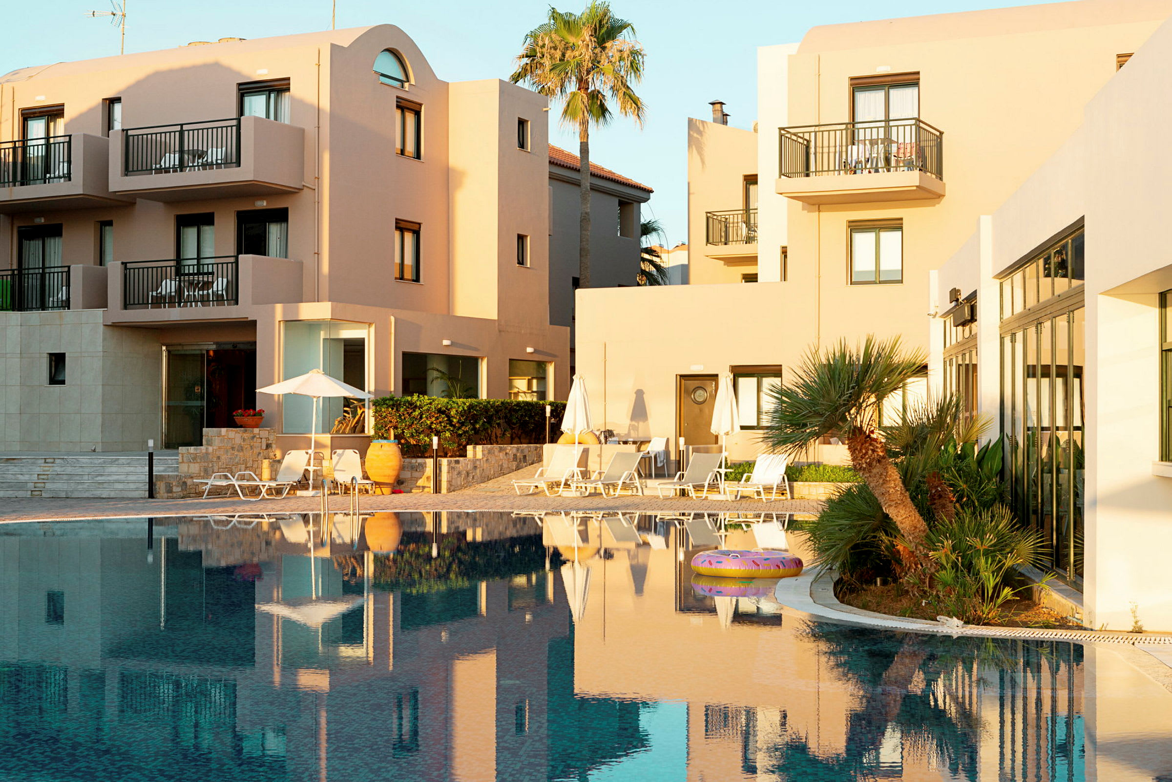 Hotelbygninger ved en pool med palmer og liggestole. (AI-genereret tekst)