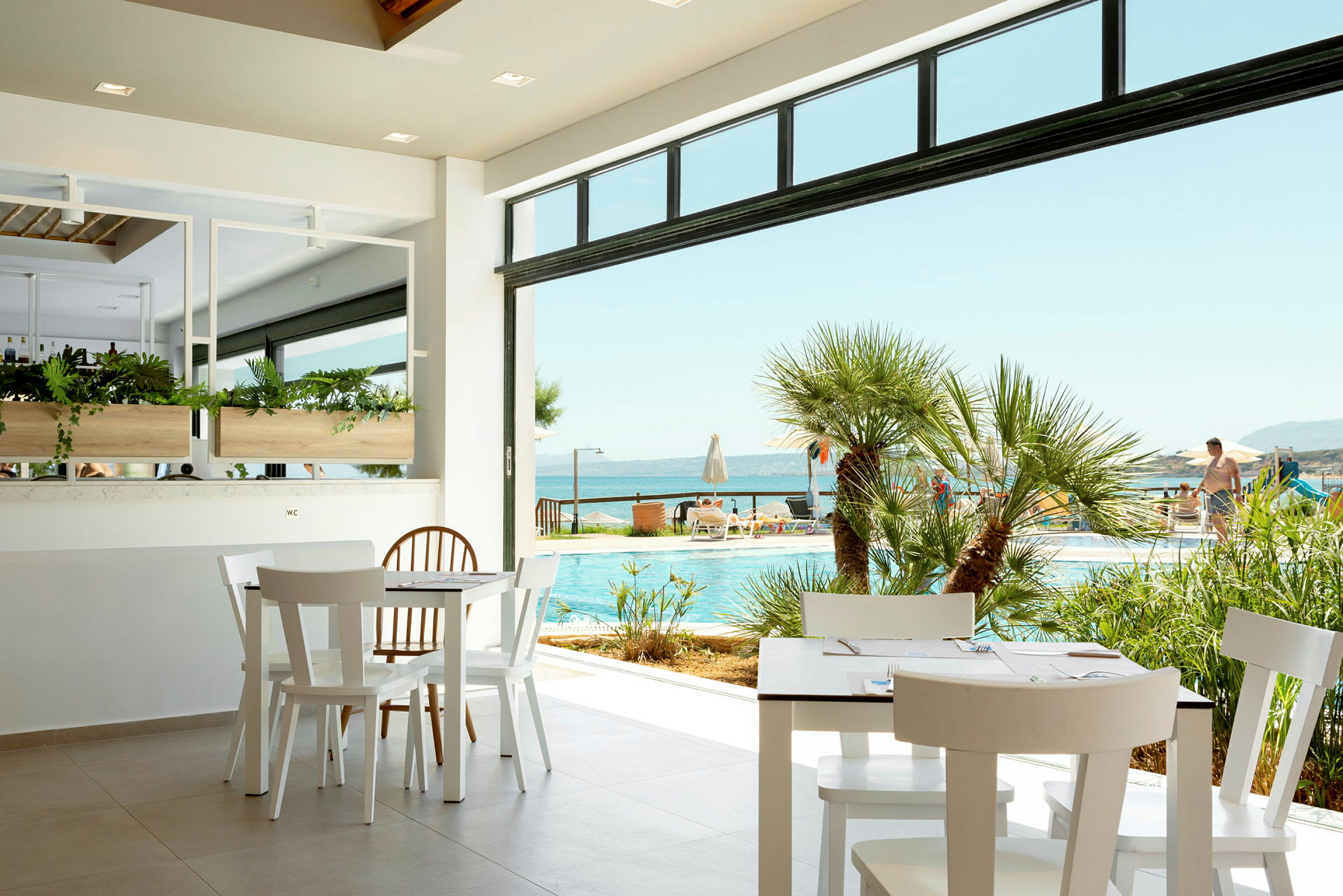 Udsigt fra en café mod en pool og havet. (AI-genereret tekst)