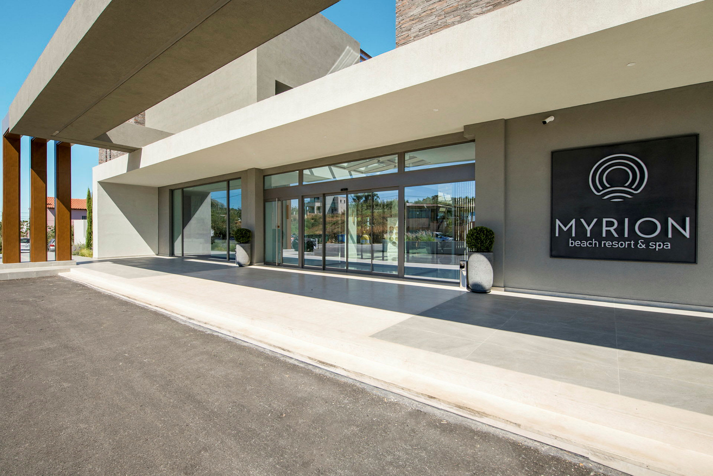 Indgangen til Myrion Beach Resort & Spa med glasvægge og et skilt. (AI-genereret tekst)