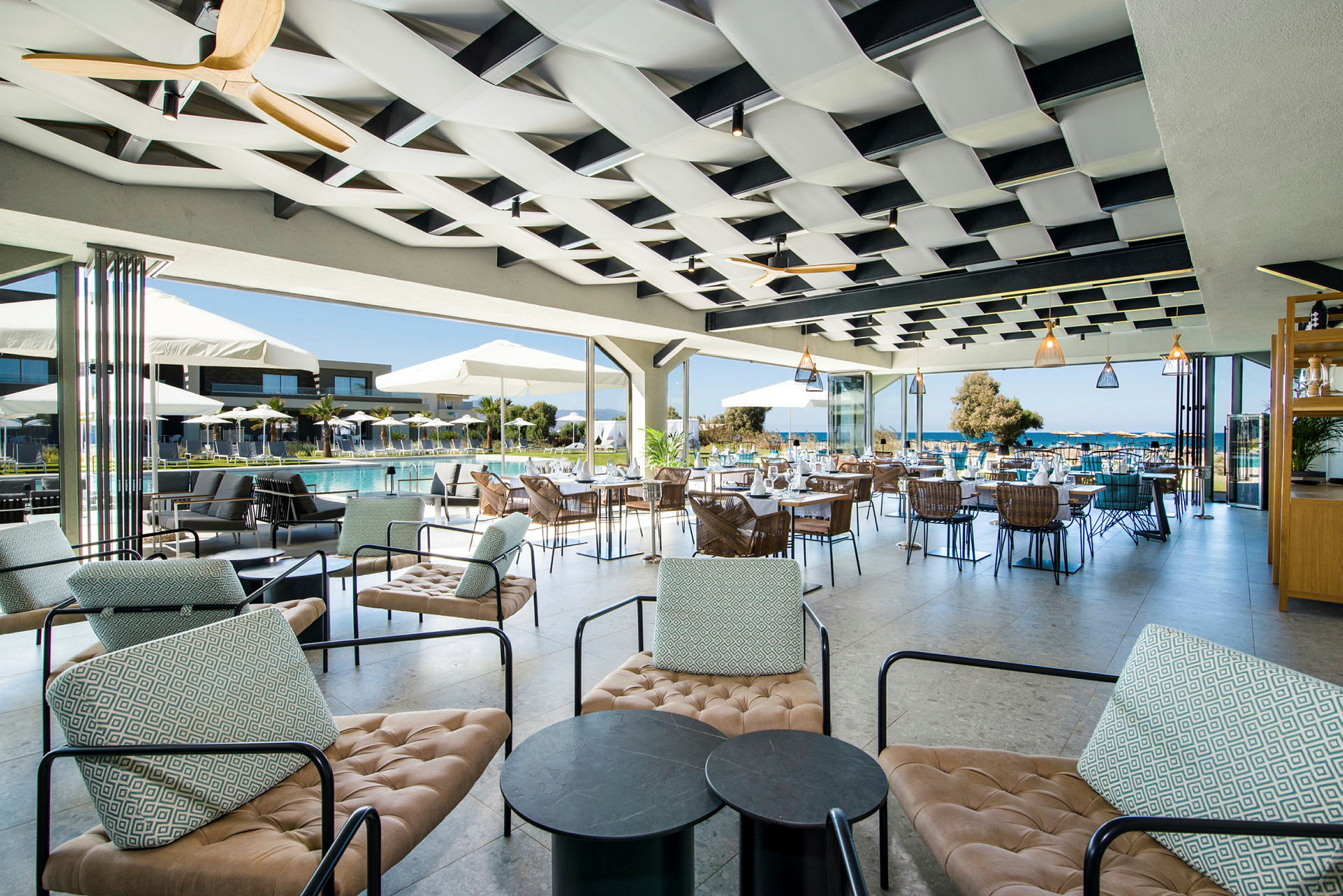 Udendørs siddeområde ved poolområdet på et hotel, med moderne møbler og udsigt over havet. (AI-genereret tekst)