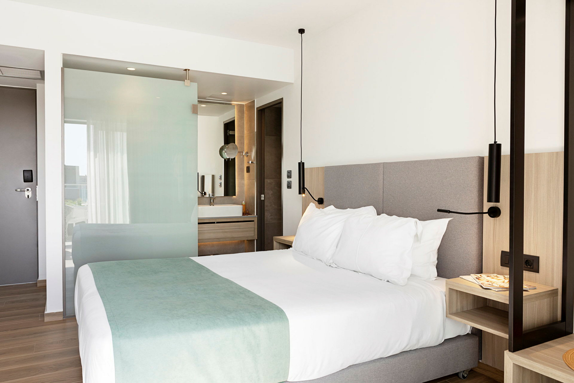 Hotelværelse med en dobbeltseng, natbord og åben planløsning mod badeværelset. (AI-genereret tekst)