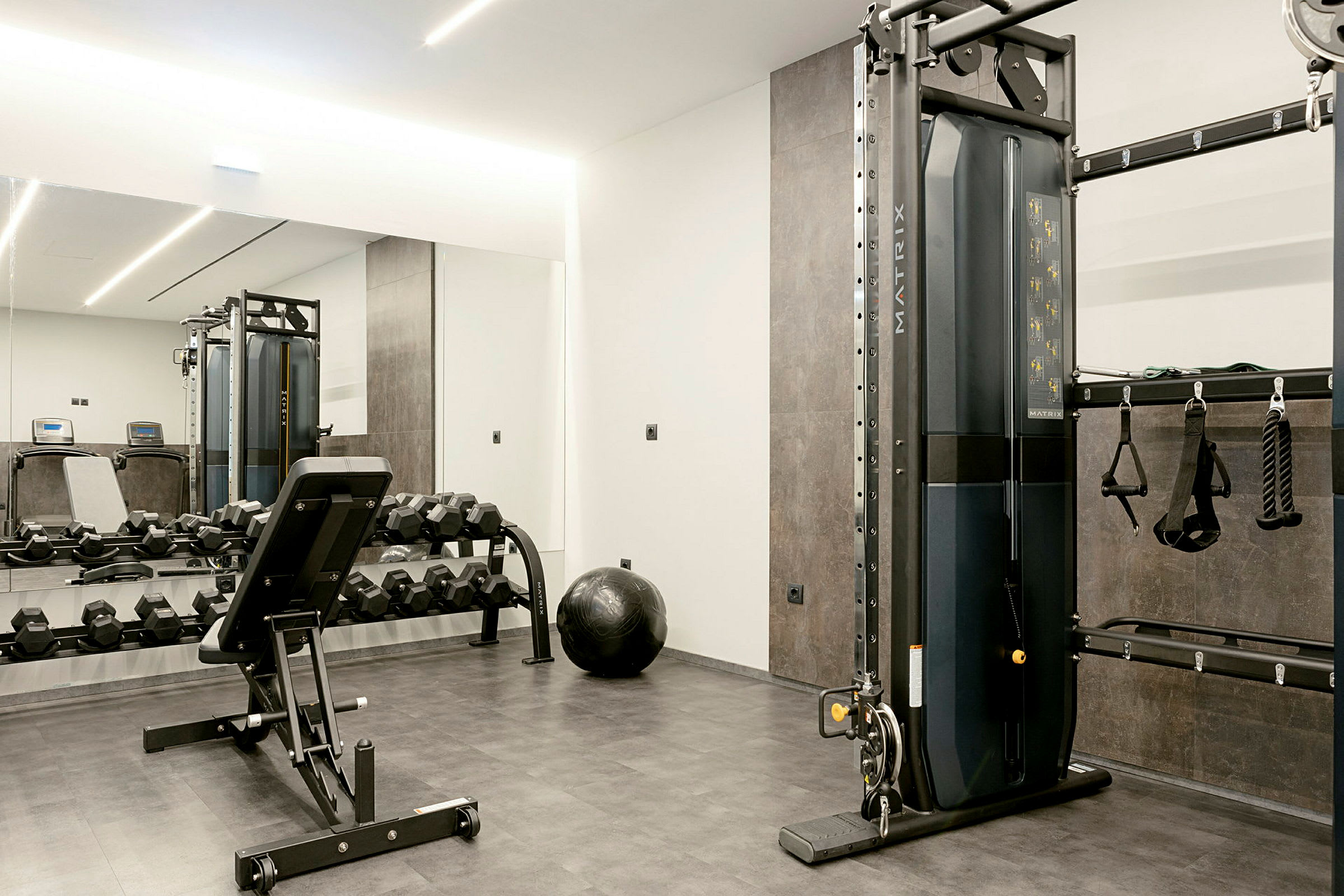 Et fitnesscenter med træningsudstyr, herunder håndvægte, en bænk og en træningsmaskine. (AI-genereret tekst)