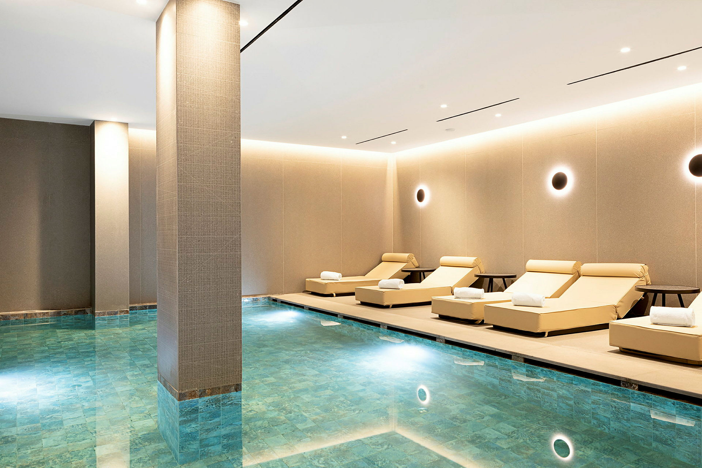 Billede af et indendørs spa med liggestole ved en pool. (AI-genereret tekst)