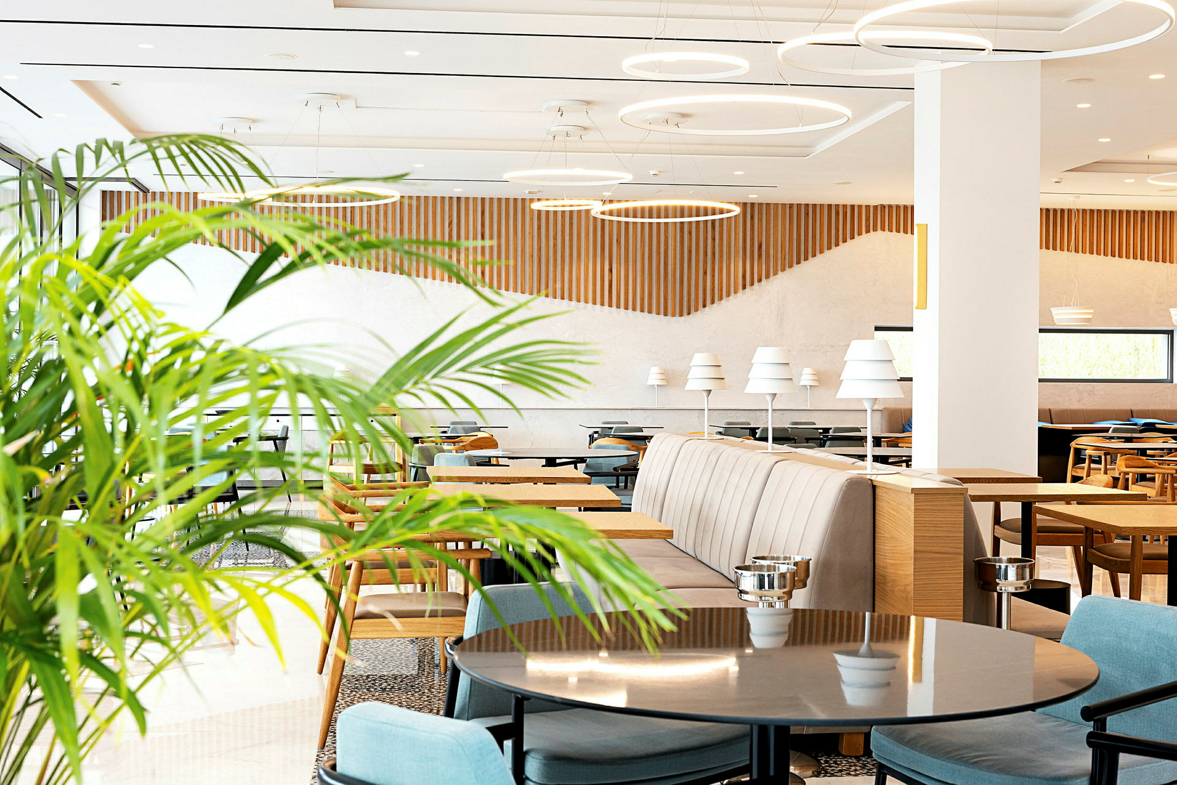 Lys og moderne restaurant med borde, stole og dekorative grønne planter. (AI-genereret tekst)