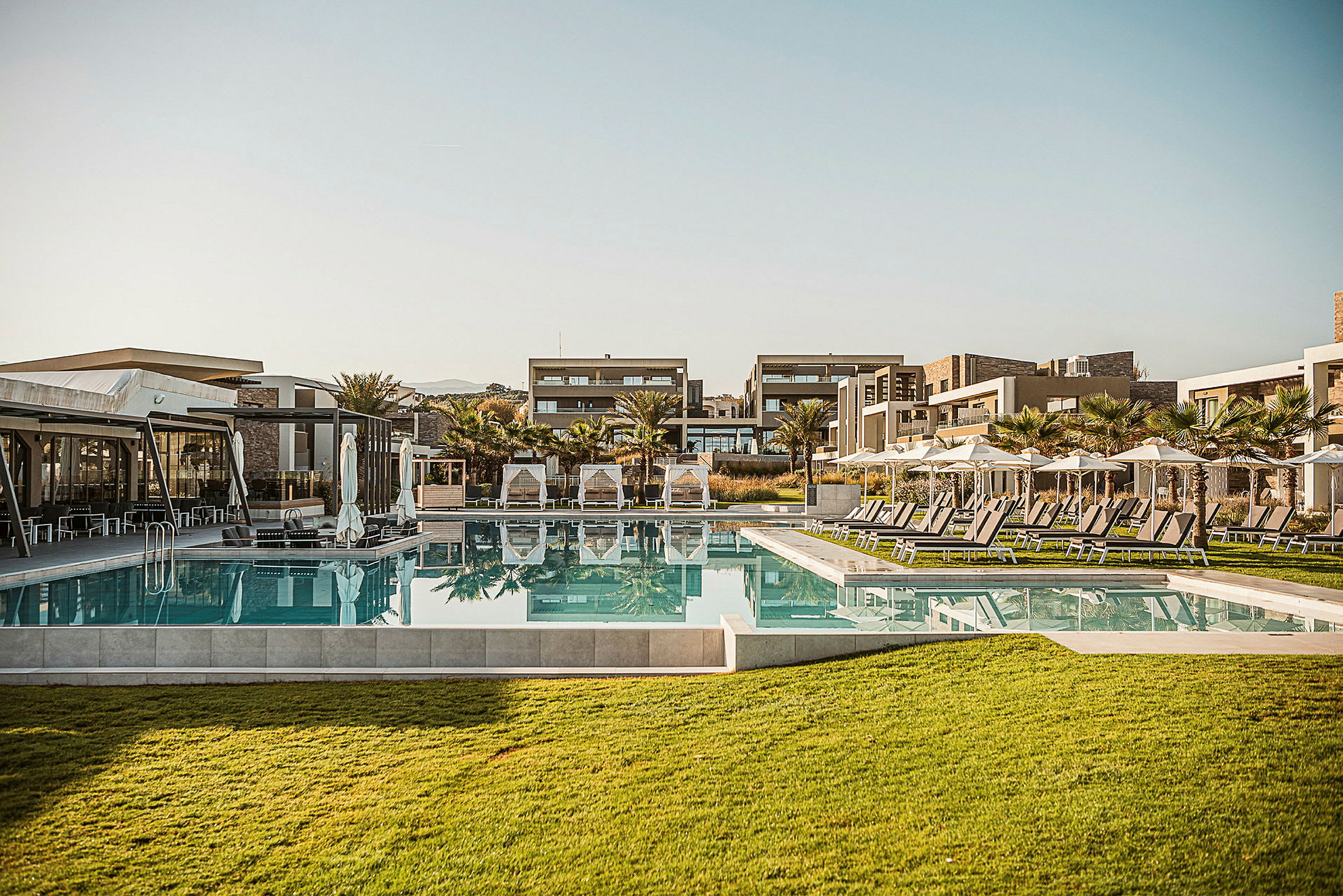 Billede af et hotelområde med pool, liggestole og moderne bygninger. (AI-genereret tekst)