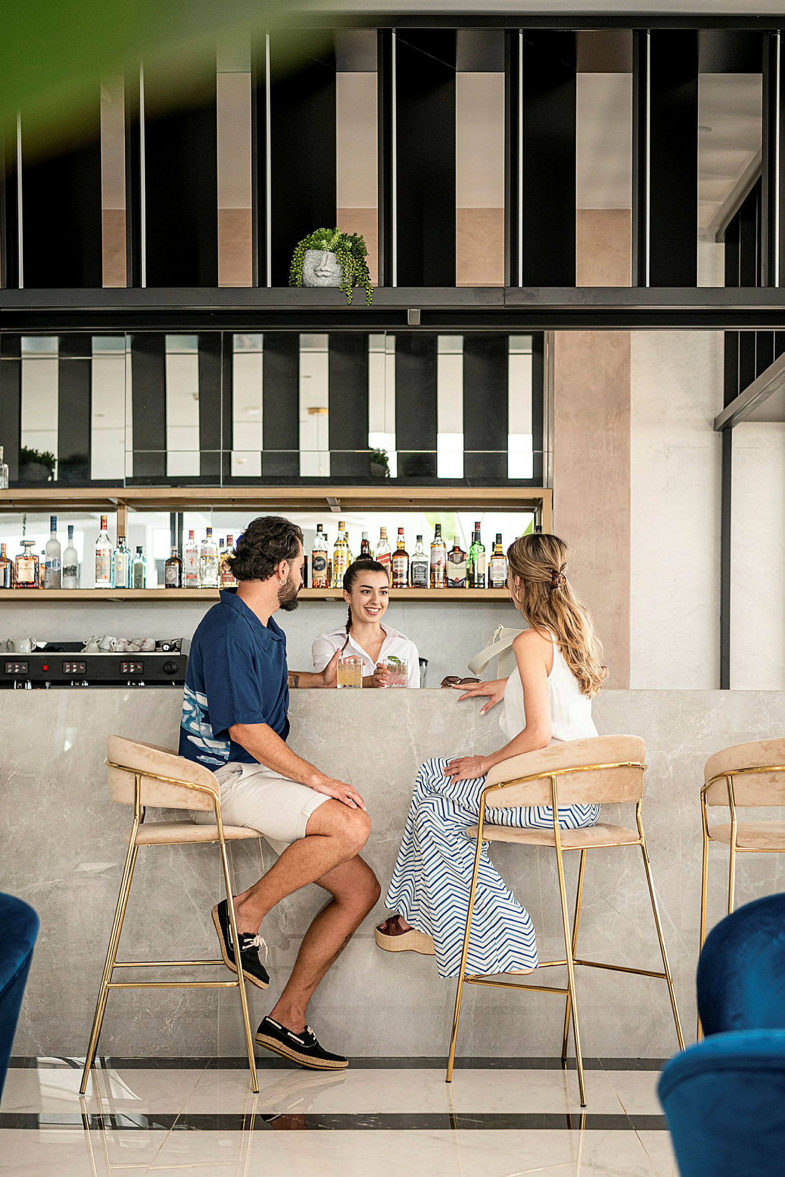 Billede af to personer siddende ved en marmordisk på en moderne bar med hylder fyldt med flasker. (AI-genereret tekst)