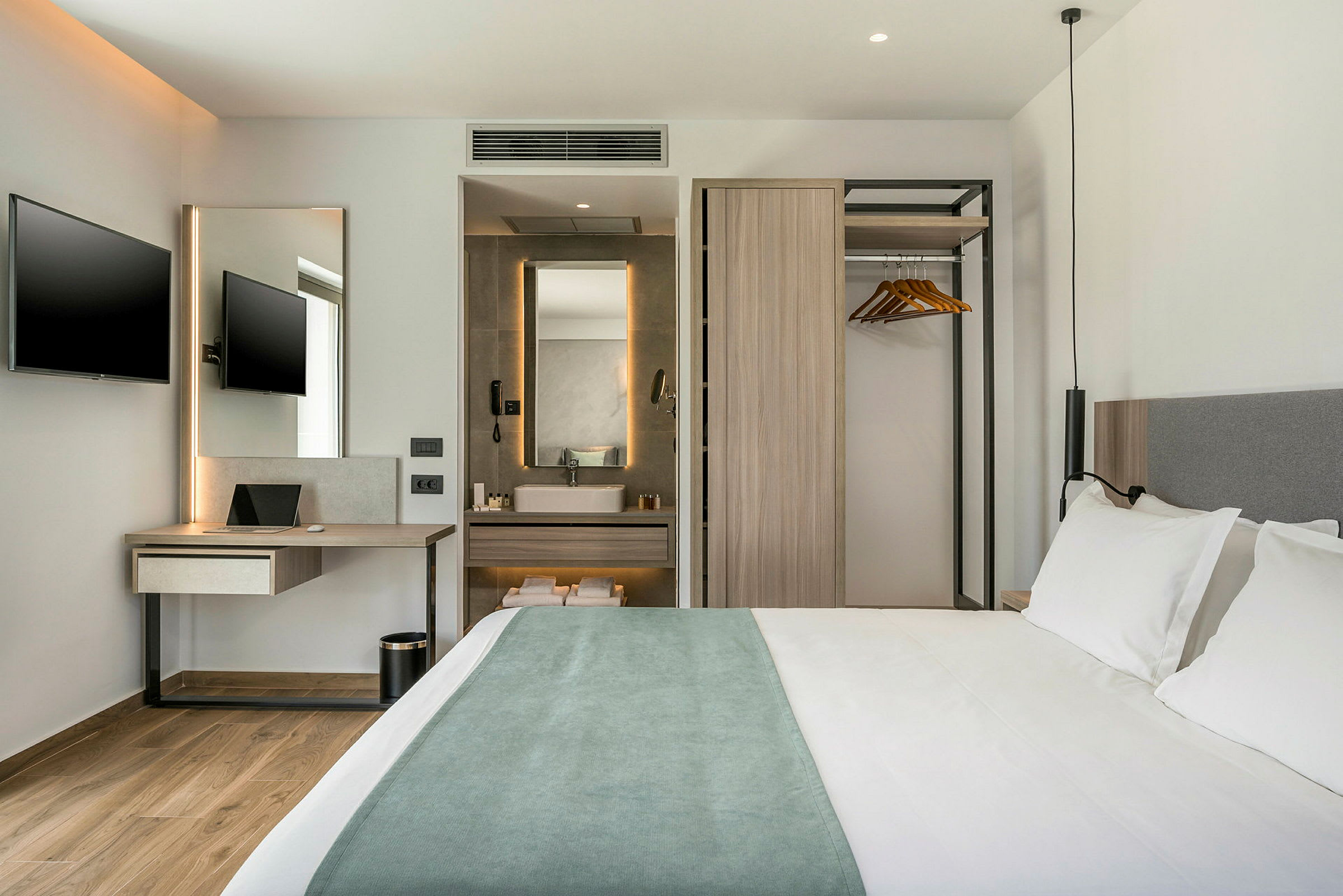 Moderne hotelværelse med dobbeltseng, skrivebord med TV samt en åben garderobe og badeværelse. (AI-genereret tekst)