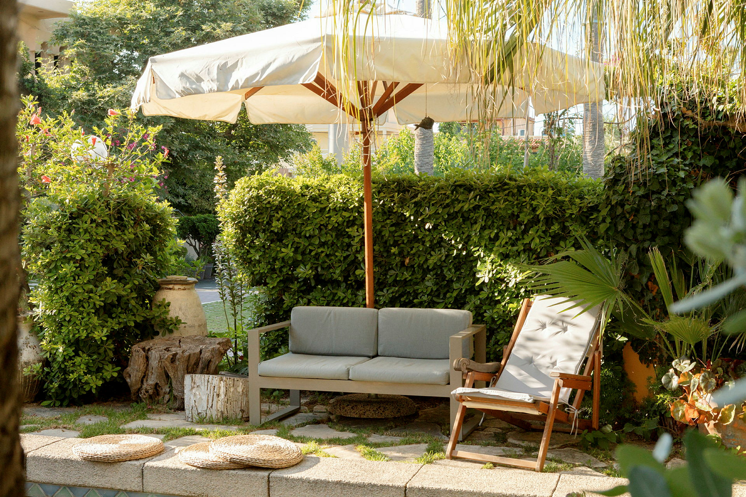 Udendørsområde med sofa, liggestol og parasol omgivet af grønt. (AI-genereret tekst)