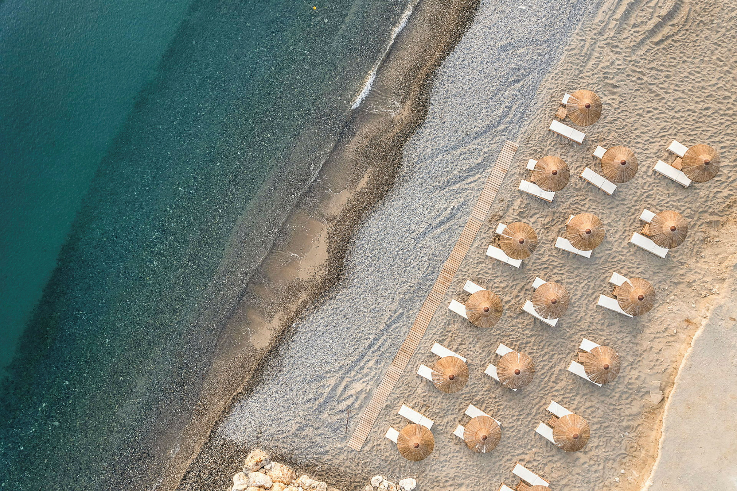 Luftfoto af liggestole og parasoller opstillet på en sandstrand tæt ved vandet. (AI-genereret tekst)