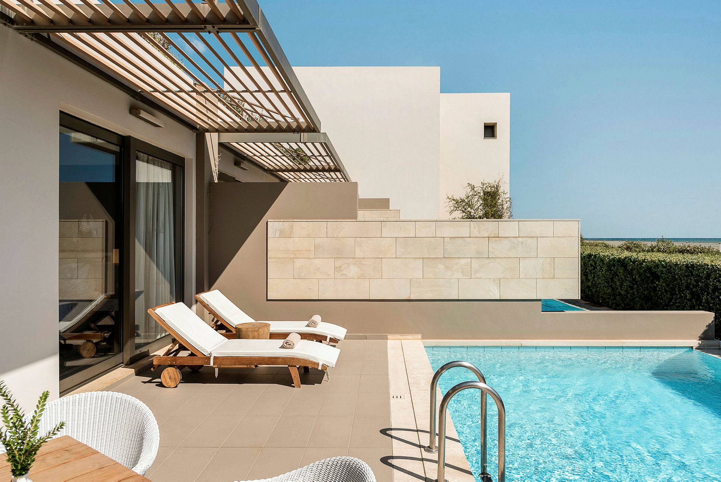 En terrasse med solsenge ved siden af en swimmingpool. I baggrunden er der en mur og himmel. (AI-genereret tekst)